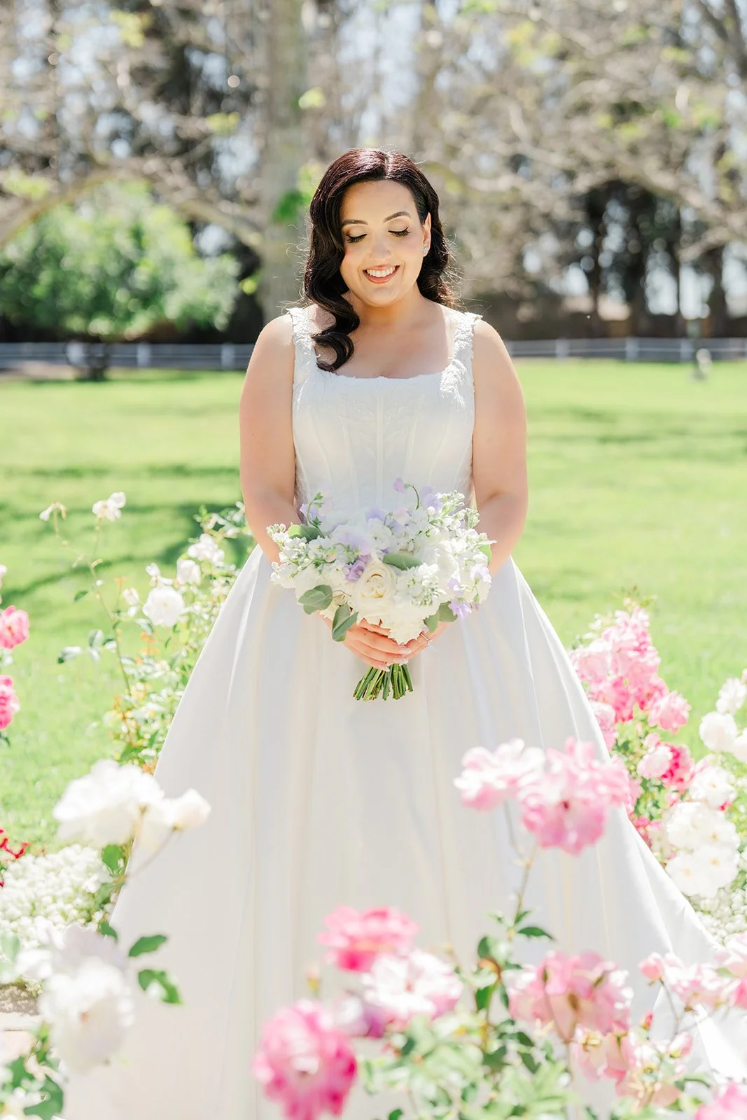 Mariam holding an ivory and lavender bouquet among pink roses