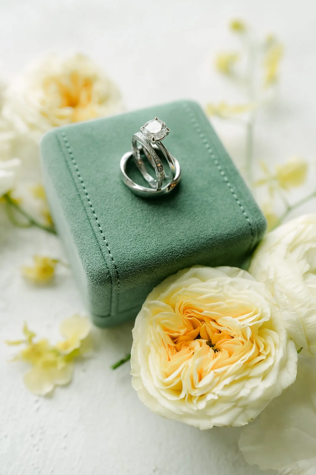 Wedding rings in a green ring box with butter yellow roses.