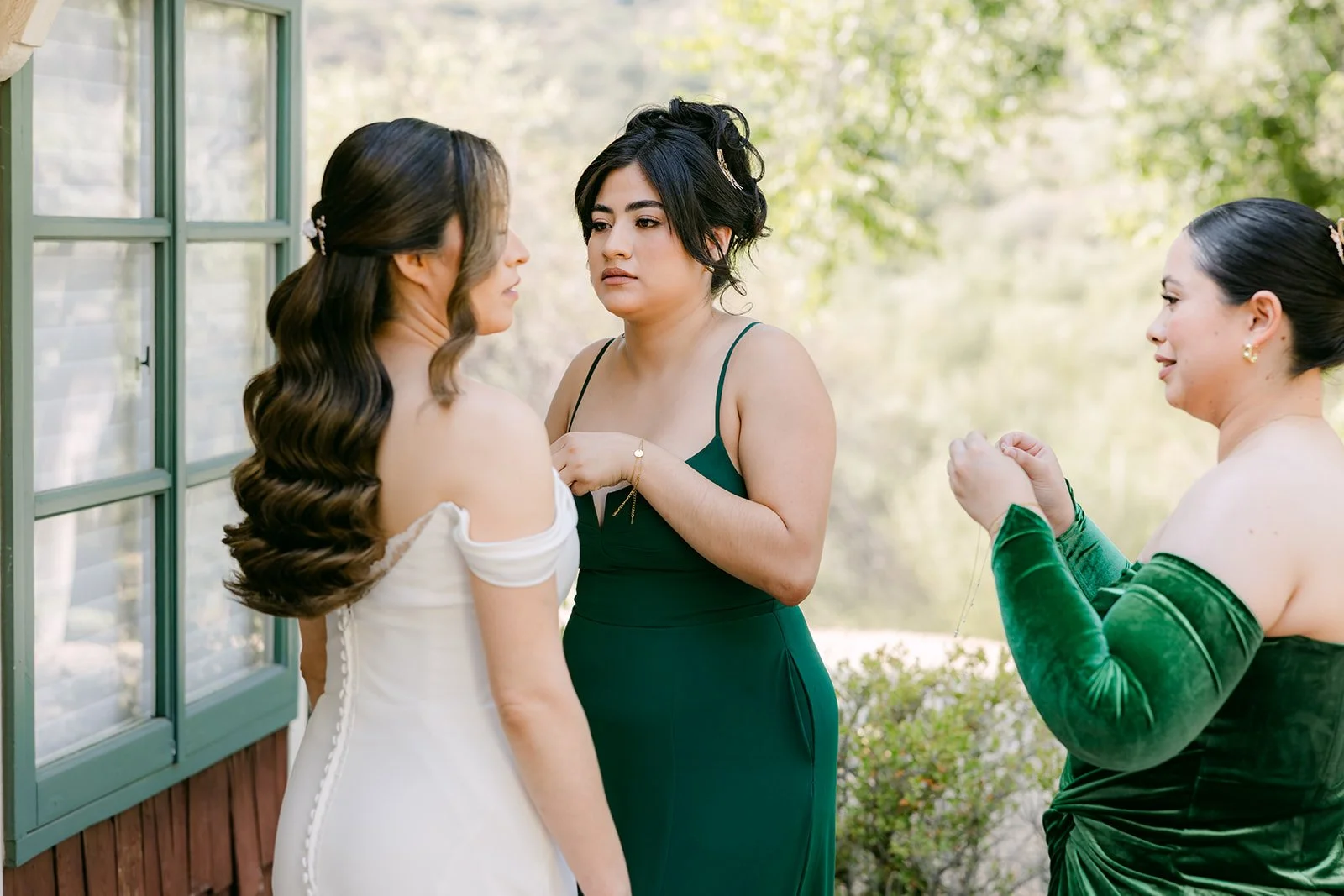 Bridesmaids in emerald green helping Mariana into her off the shoulder gown