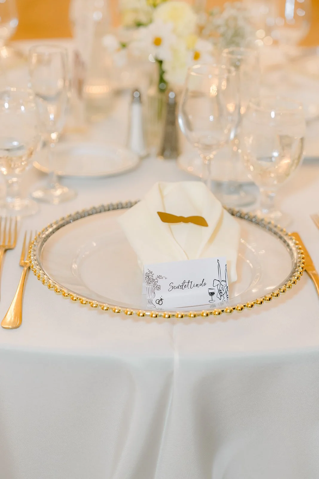 Place setting with a gold charger, menu card and white florals.