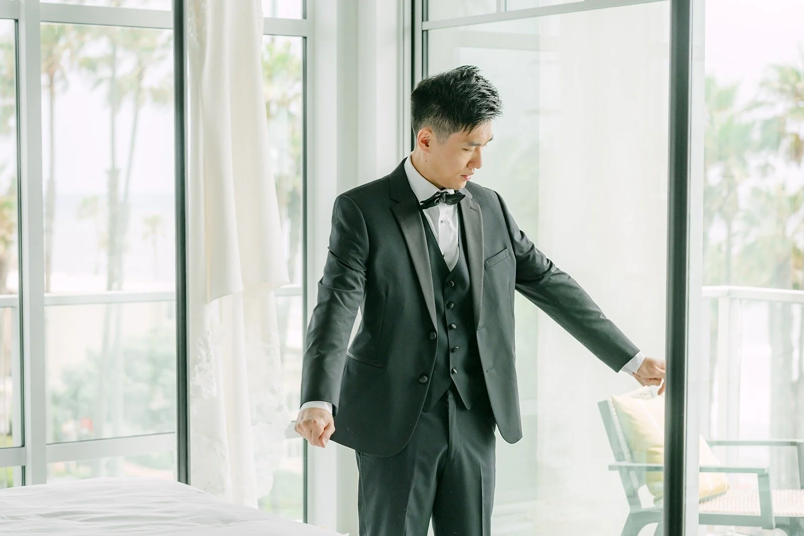 Eli putting on his jacket by the window in the groom's suite