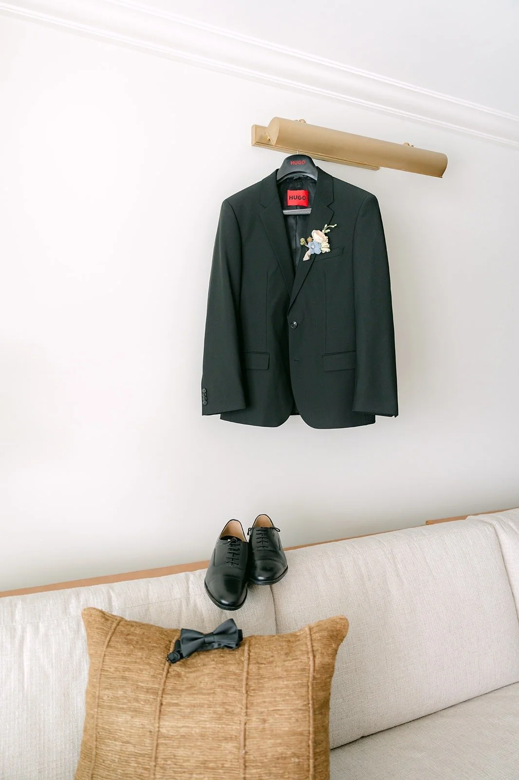 Mario's black tuxedo hanging on the wall above his dress shoes