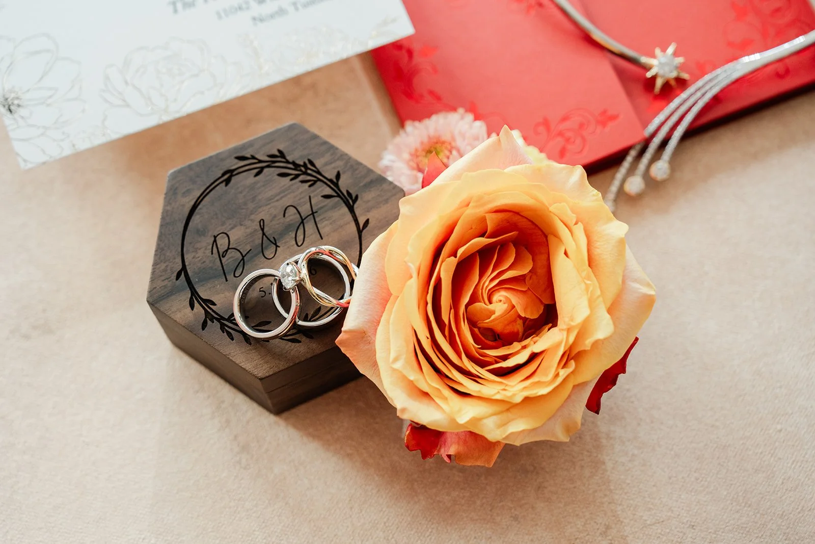 Wedding rings in a dark ring box beside a peach rose.