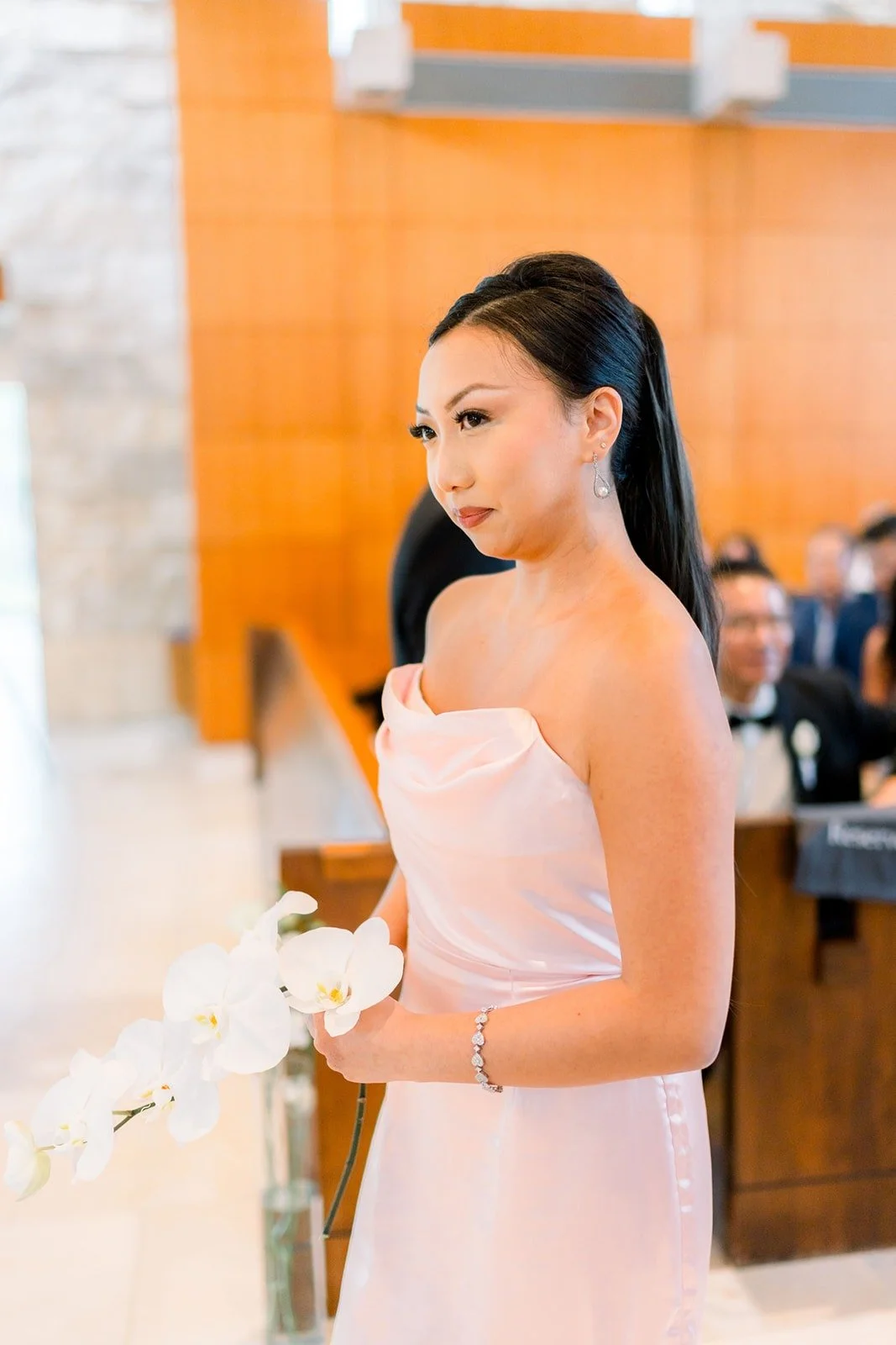 A bridesmaid in blush walks down the aisle with white orchids