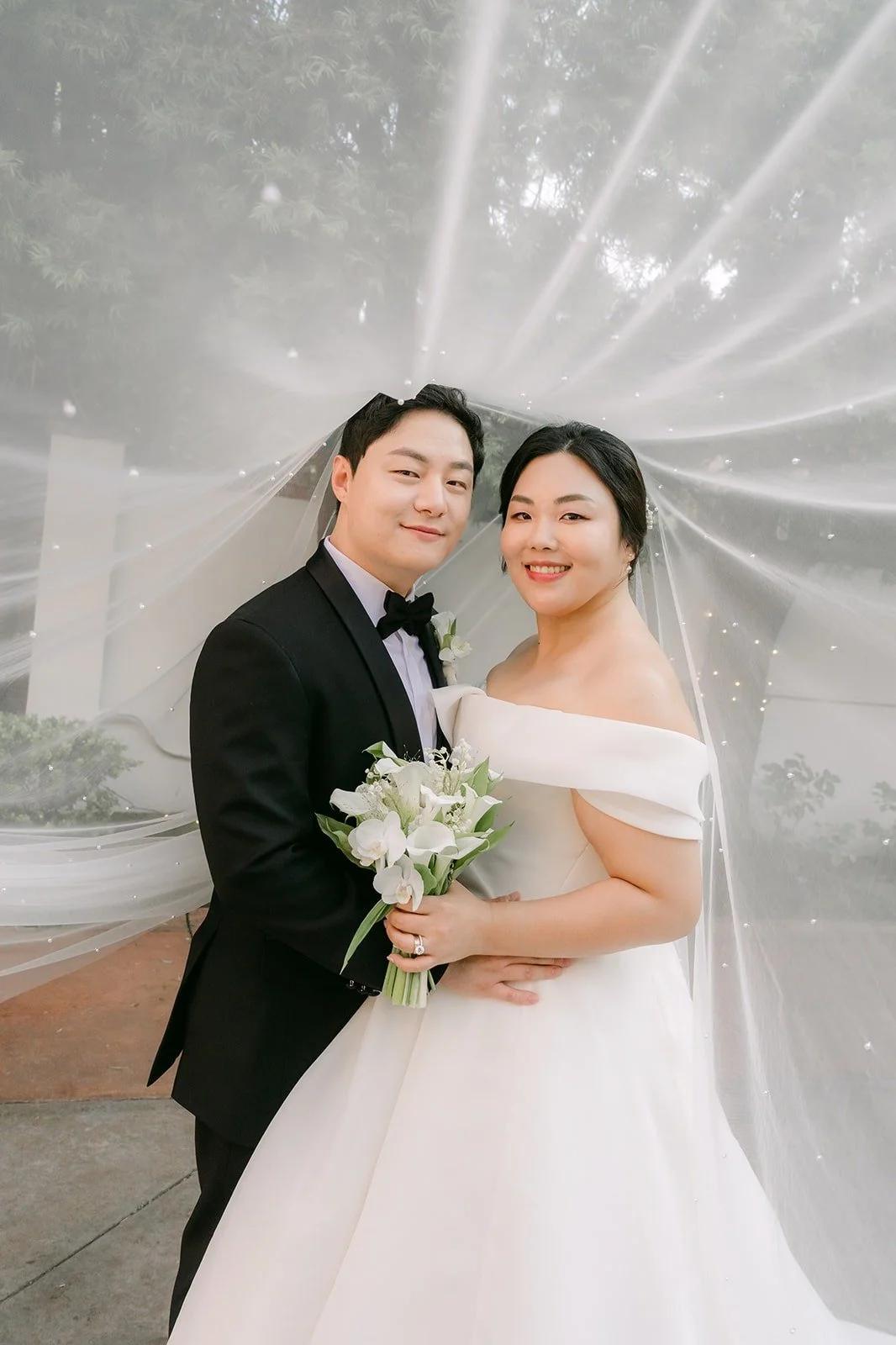 Chorok and Min Soo smiling under the veil at Franciscan Gardens, photographed by One and Only Production