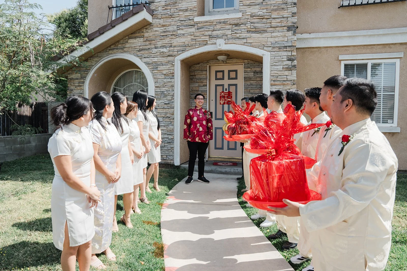 Groomsmen carrying red gift trays up the front walk.