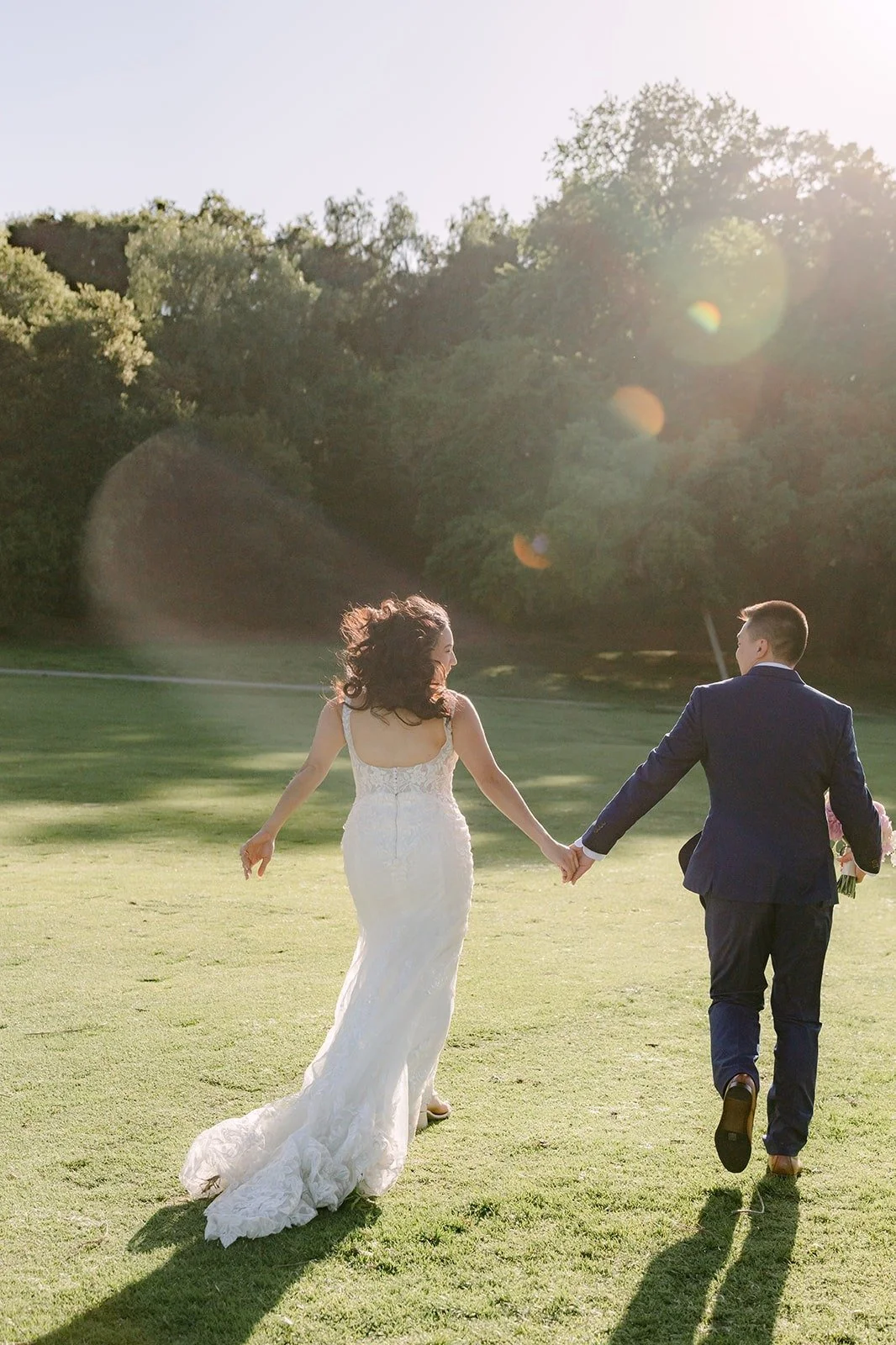 Kelli and Alex walking hand in hand across the lawn toward the sun at Los Robles Greens