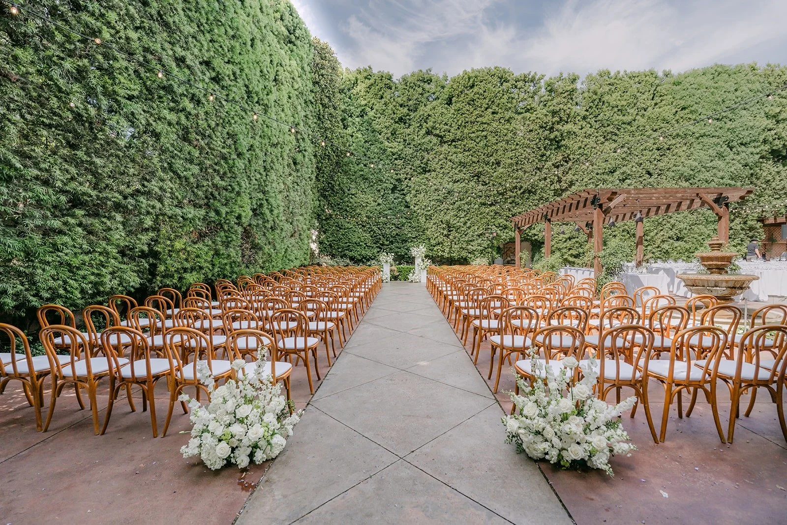 The ceremony aisle at Franciscan Gardens lined with white flowers and tall hedge walls