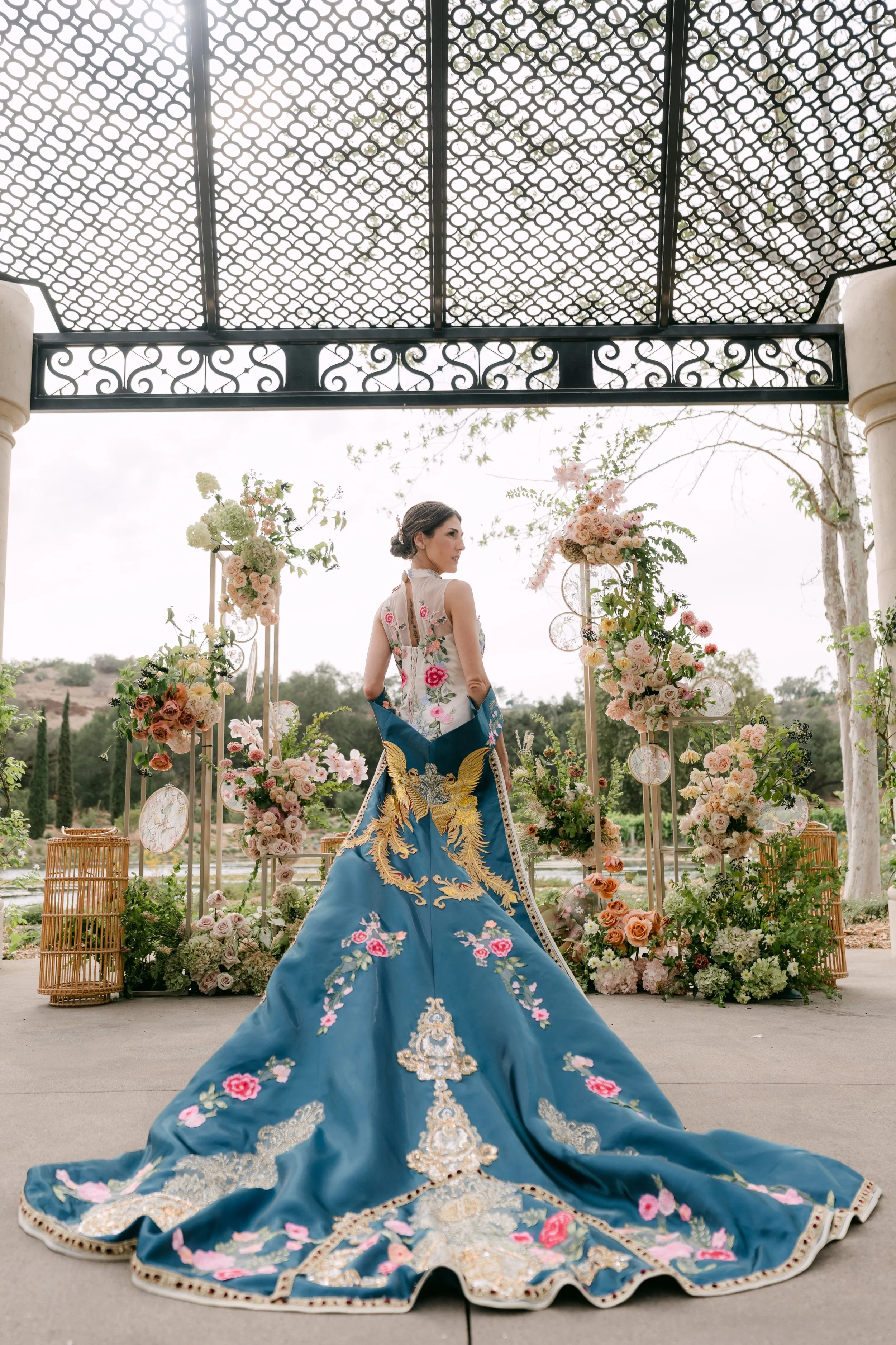 Bride in a blue embroidered gown with a sweeping train under a pergola at Monserate Winery