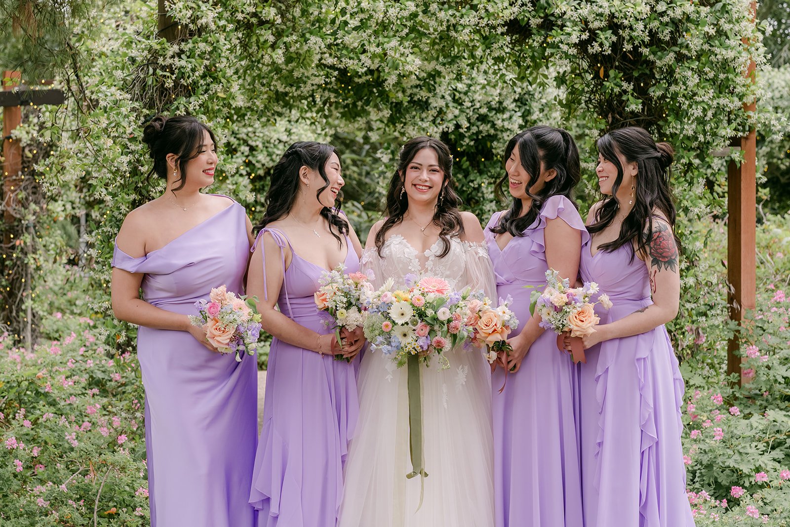 Kat with her bridesmaids in lavender gowns under an ivy arch