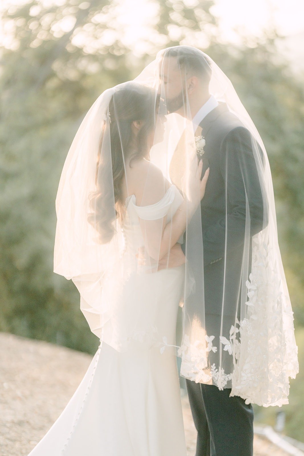 Mariana and Danny sharing a kiss beneath her veil in warm afternoon light