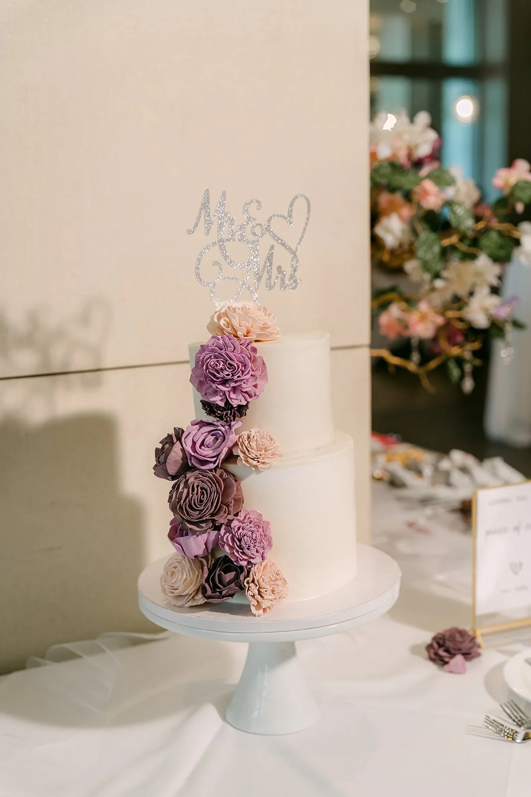 White cake with purple florals and a Mai and Bobby topper.