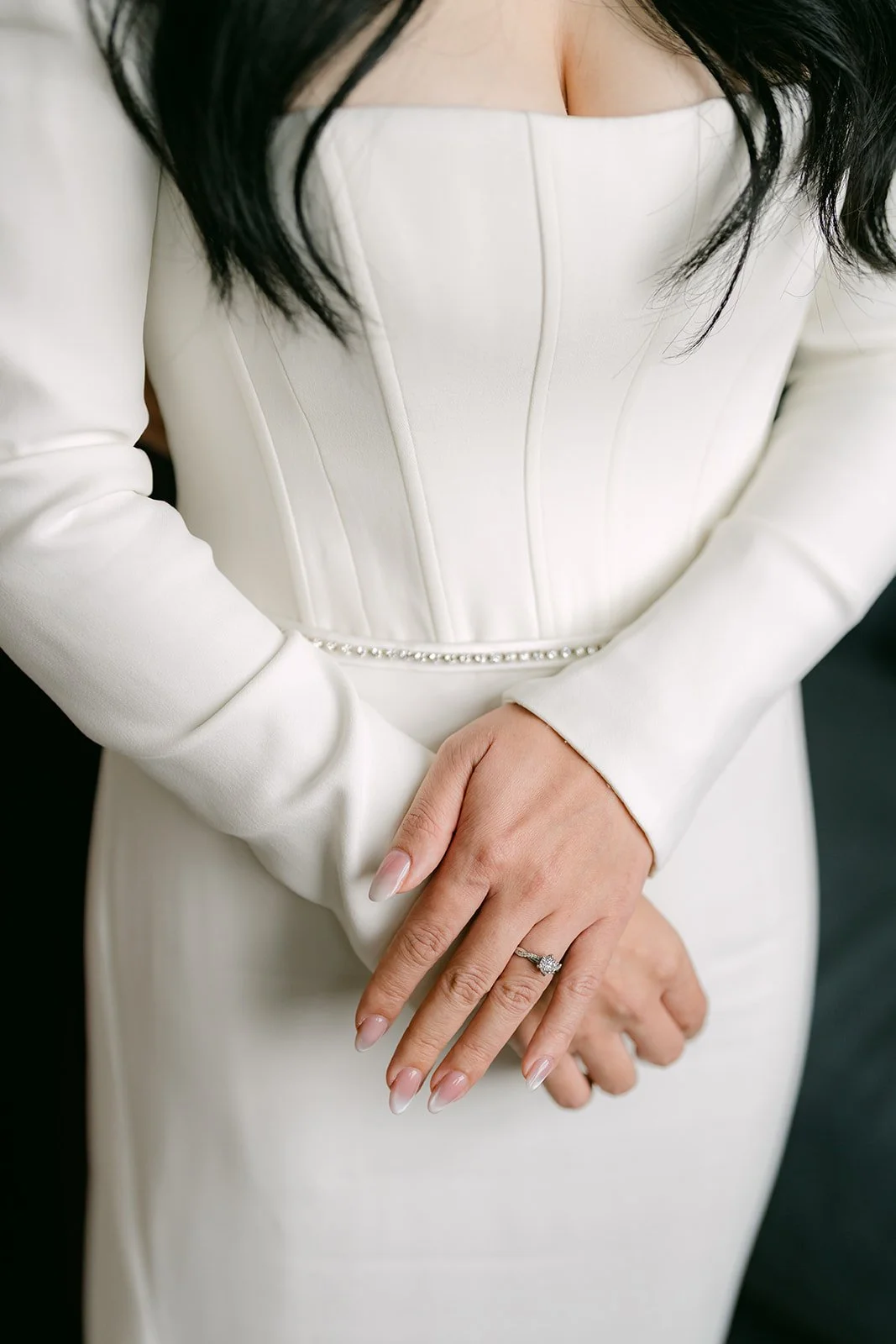 Denise's hands folded in front of her structured bodice, engagement ring on.