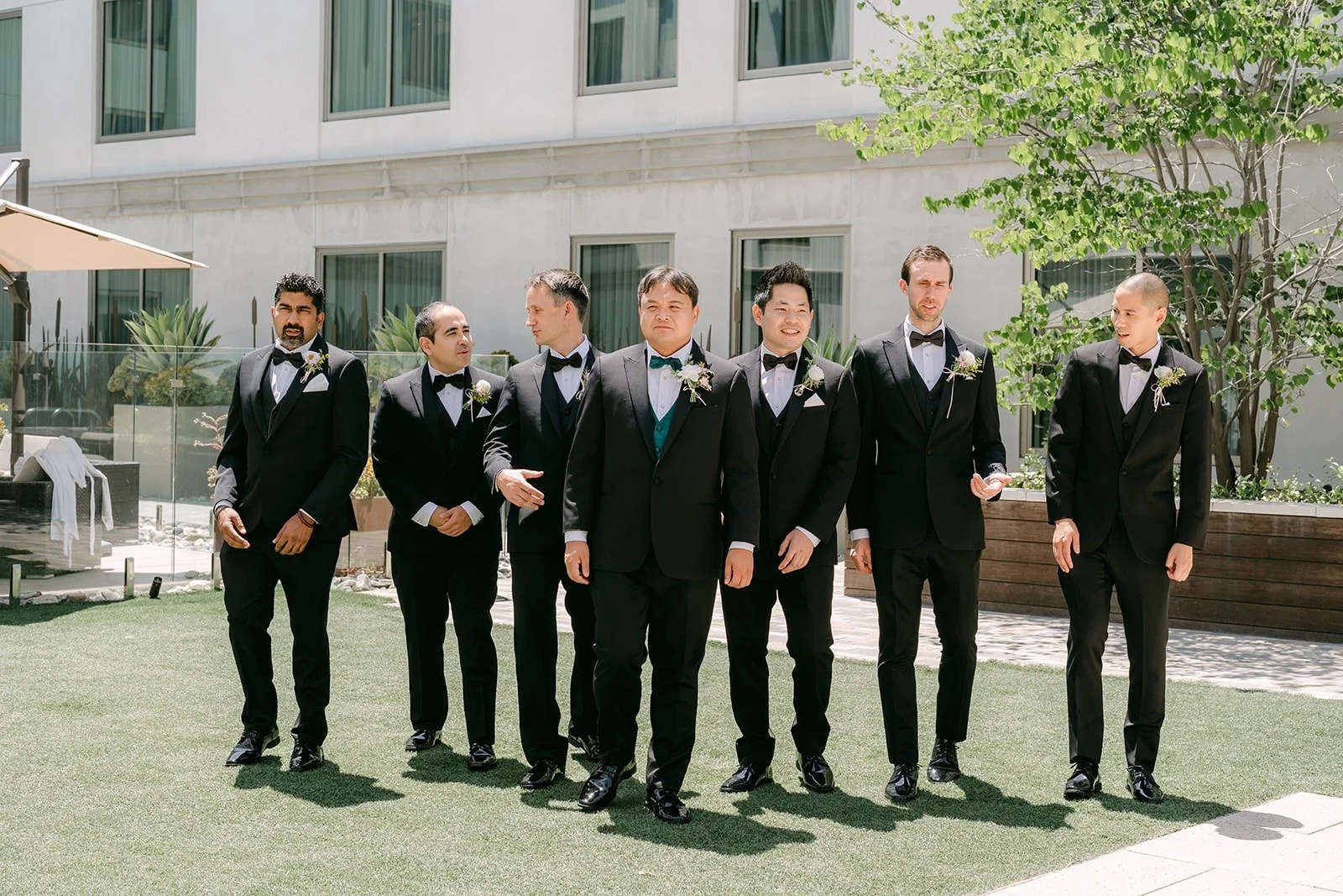 James and his groomsmen in black tuxedos lined up on the courtyard lawn at the Sheraton Los Angeles San Gabriel