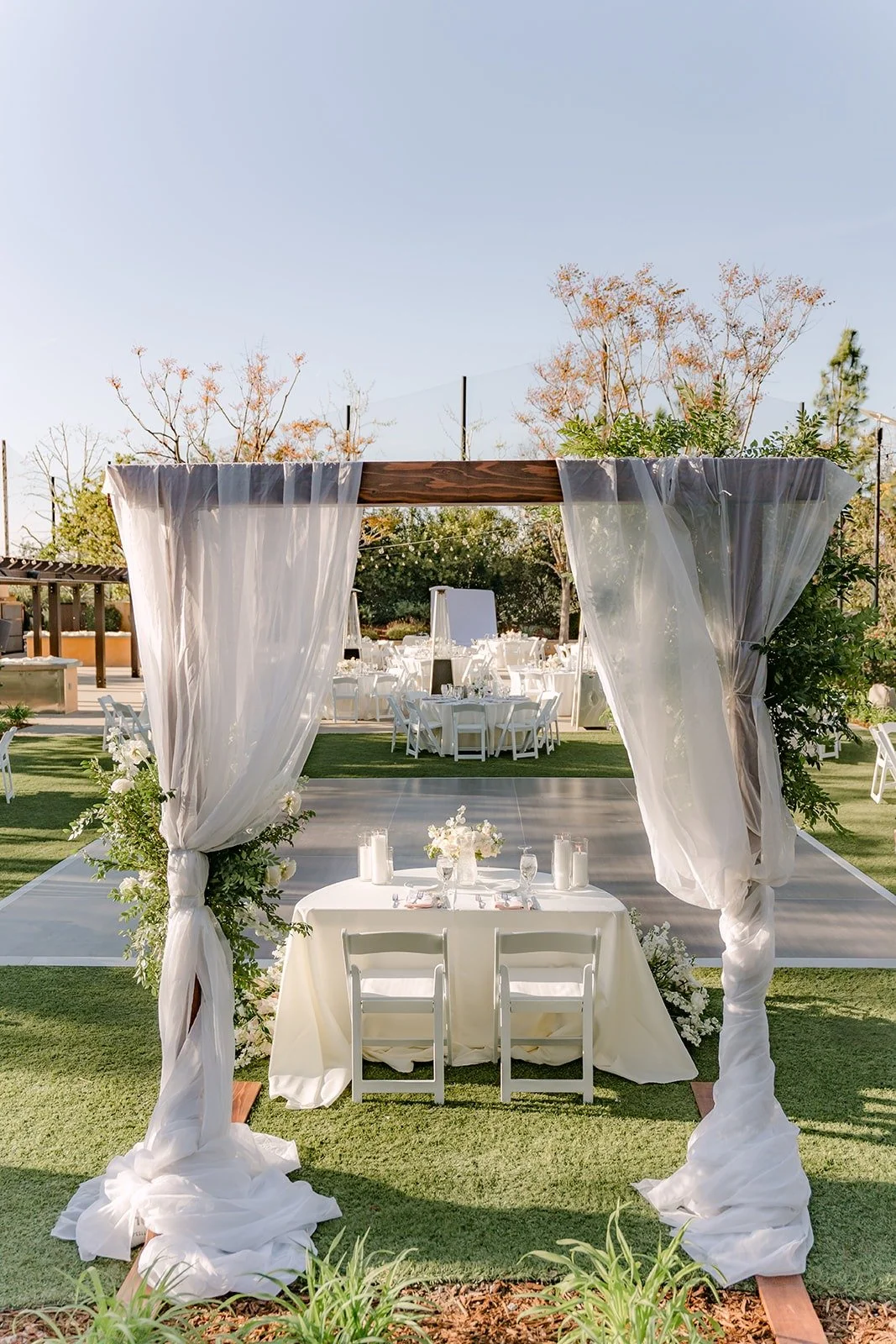 The draped sweetheart table on the lawn with the reception tables behind it