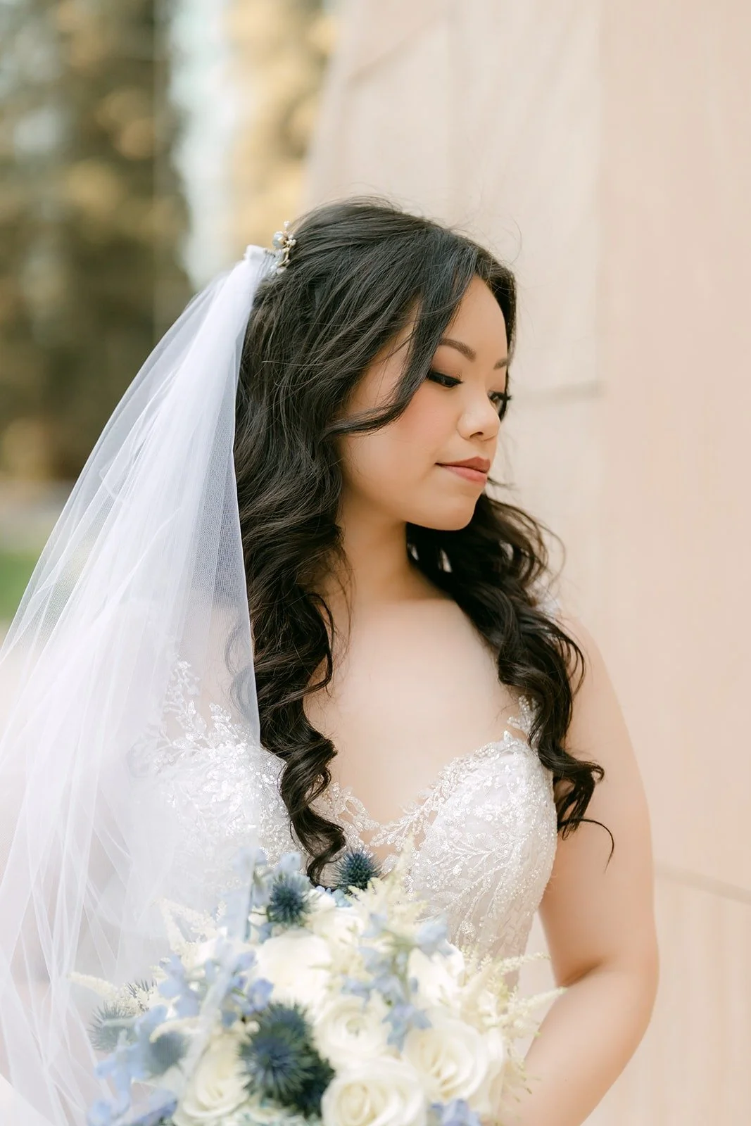 Emily under her veil holding a white and blue thistle bouquet