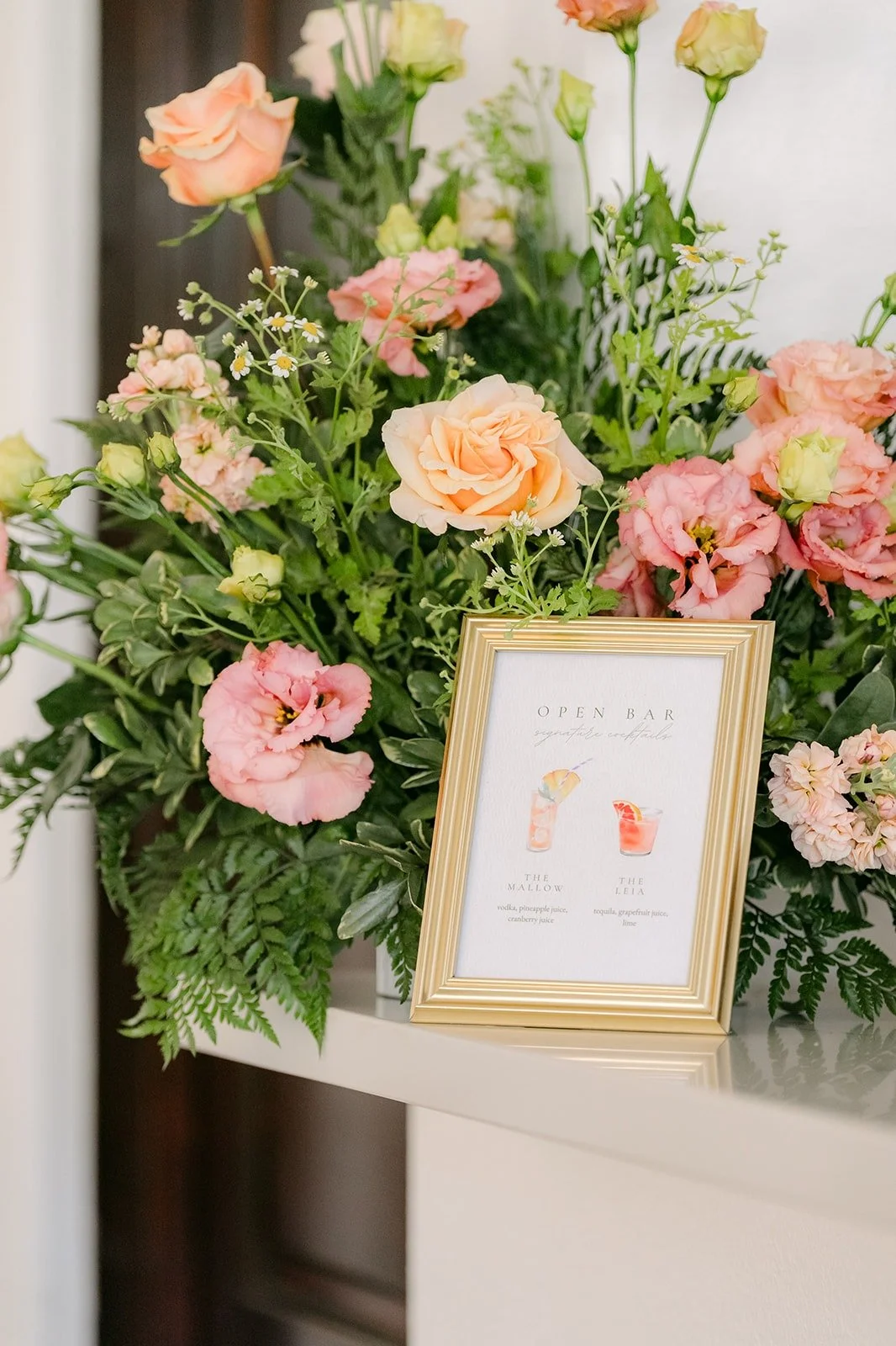 A framed sign set in a large arrangement of pink and peach flowers, photographed by One and Only Production