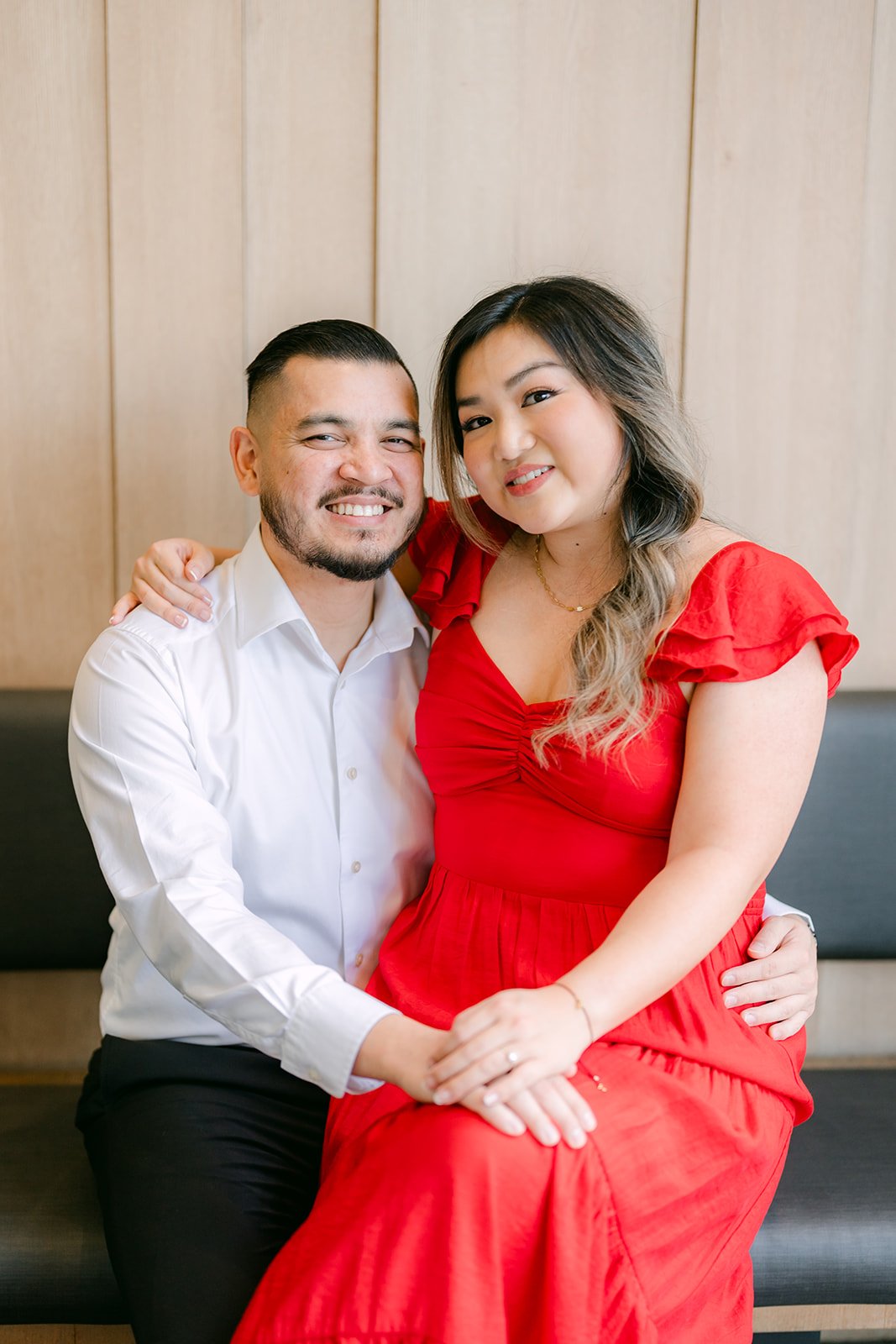 Linh and Ankush seated together on a bench in front of the wood-paneled wall.