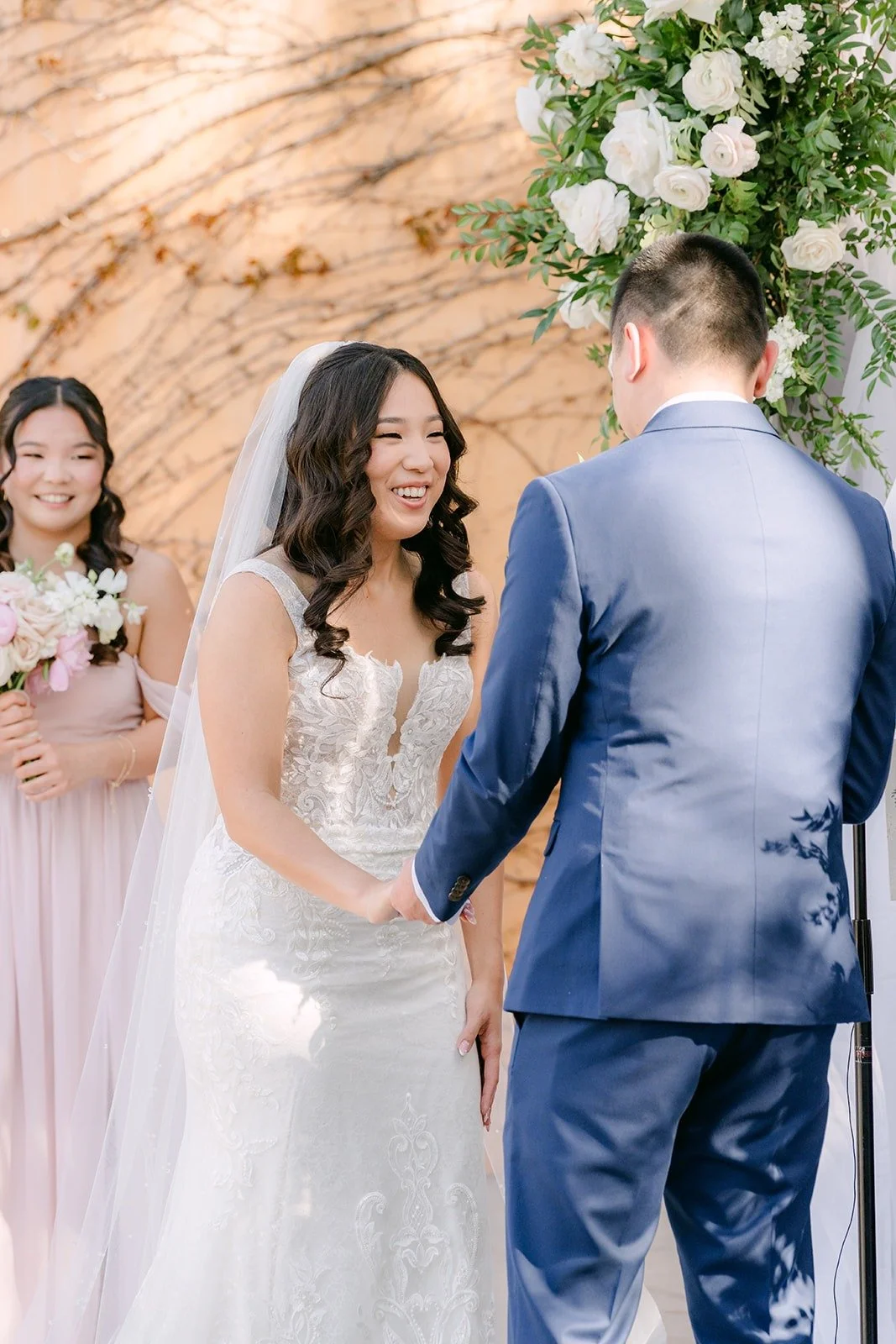 Kelli and Alex holding hands at the floral arch during the ceremony