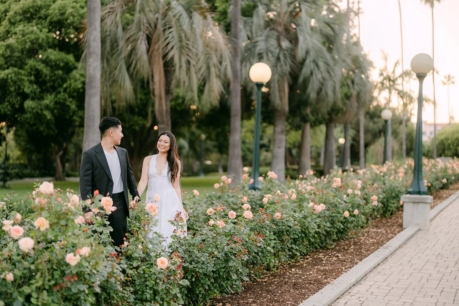 Jadee and Richard walk through the rose garden beneath tall palm trees.