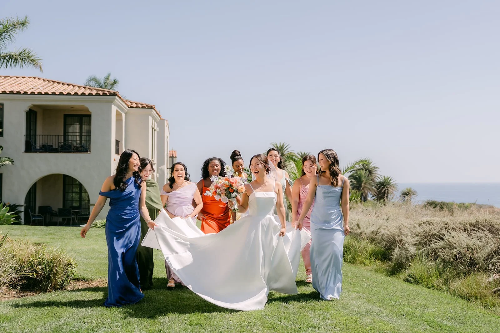 Bridesmaids carrying Saya's train across the lawn