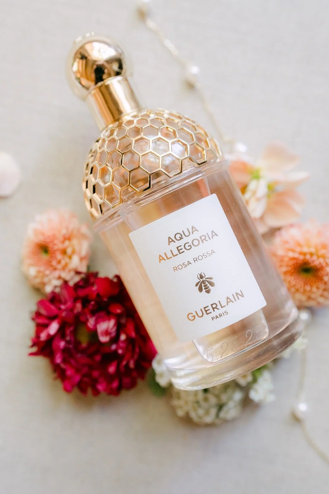 A bottle of perfume styled with red and peach blooms on a cream flatlay