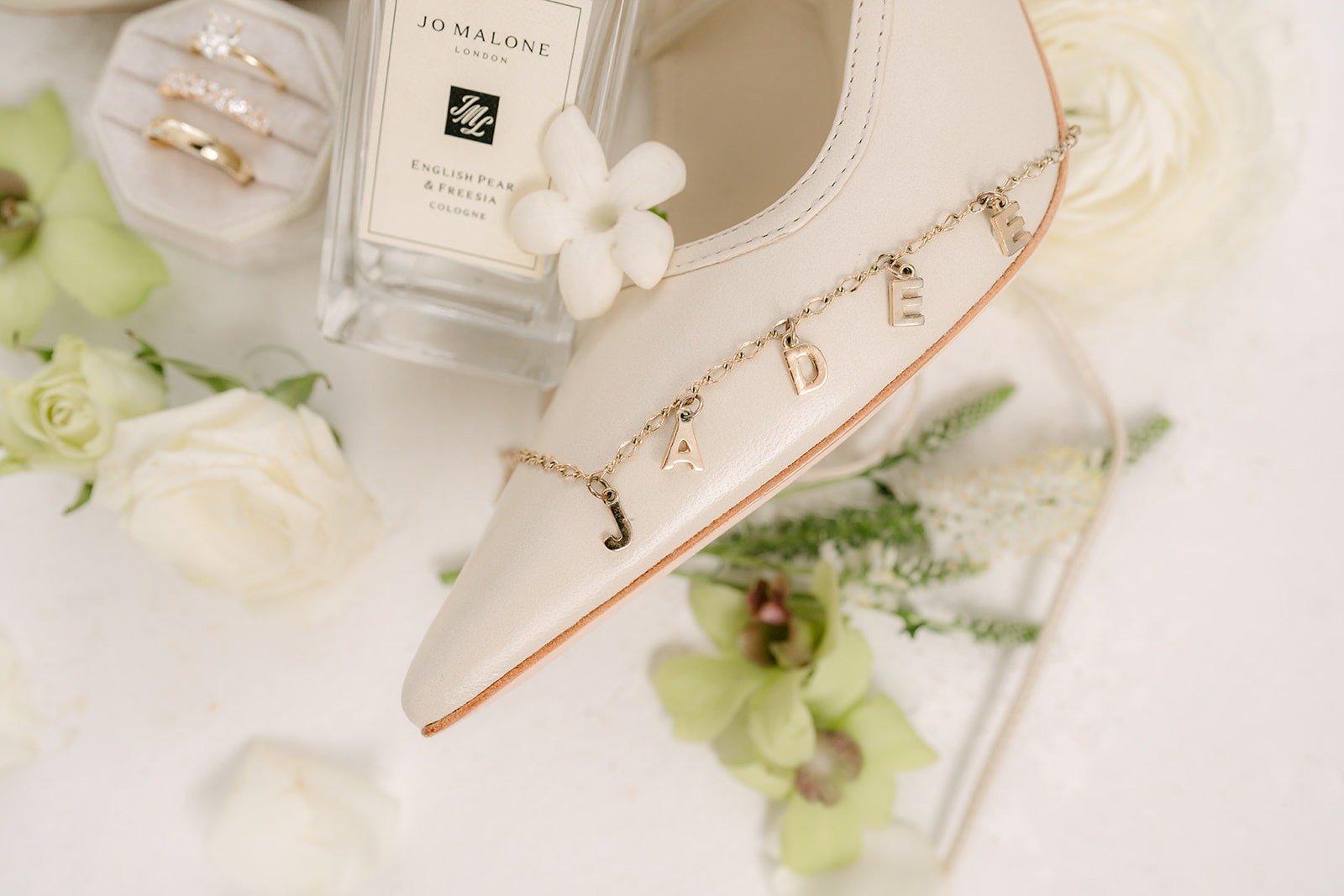 Wedding rings, perfume and white bridal heels with green orchids