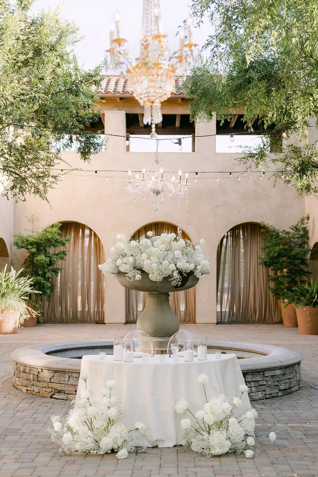 Sweetheart table with white flowers in front of the courtyard fountain