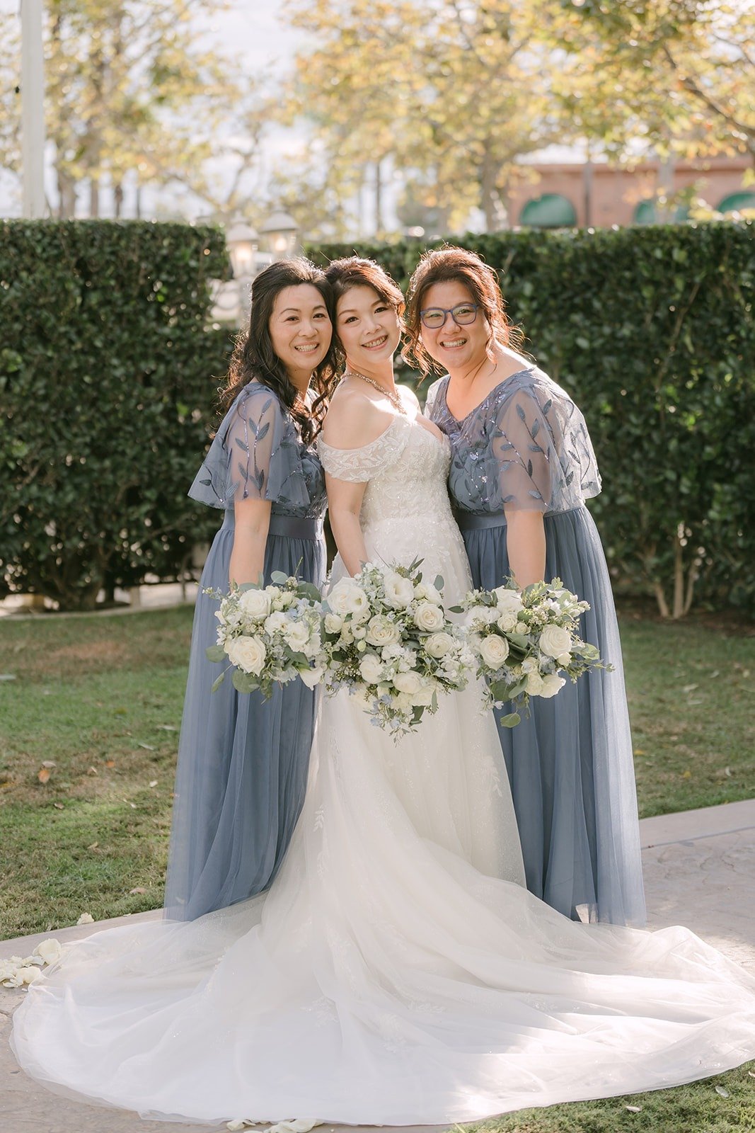 Sochi with Bonnie and Rani in dusty blue dresses in front of a green hedge