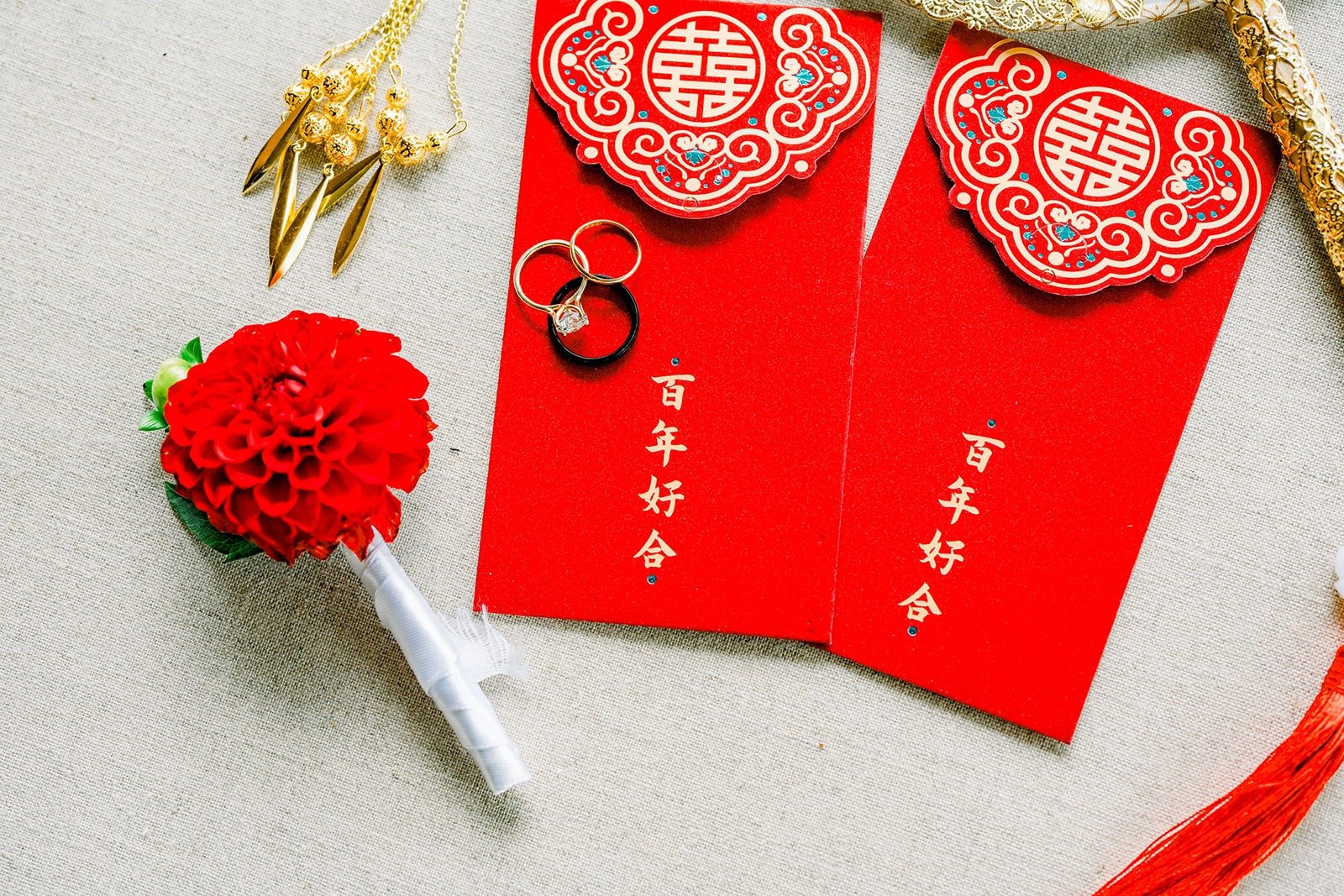 Red envelopes with paper cut designs beside a red boutonniere, photographed by One and Only Production