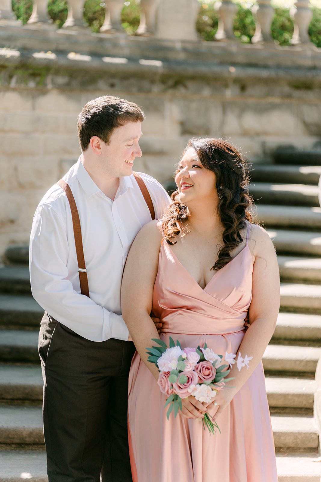 Saira and Matthew laughing together on the staircase with her bouquet.