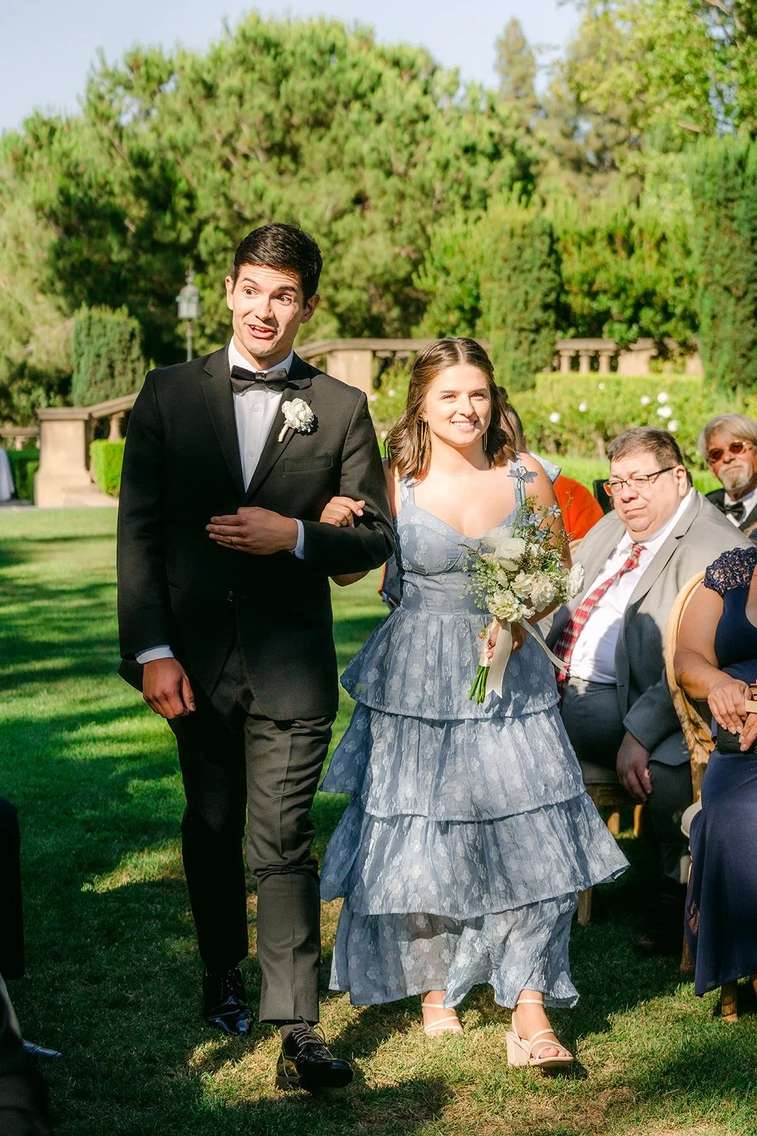 A bridesmaid in a tiered blue gown walking in with a groomsman