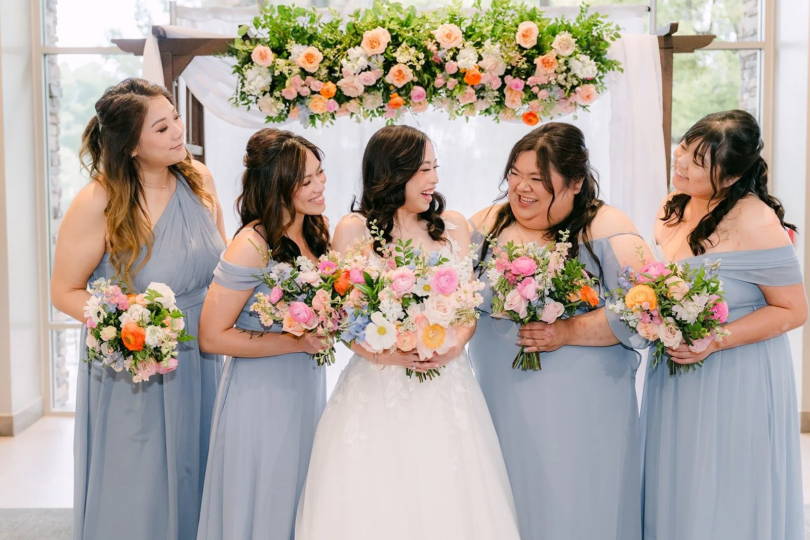 Natalie laughing with her bridesmaids in front of the floral ceremony arch