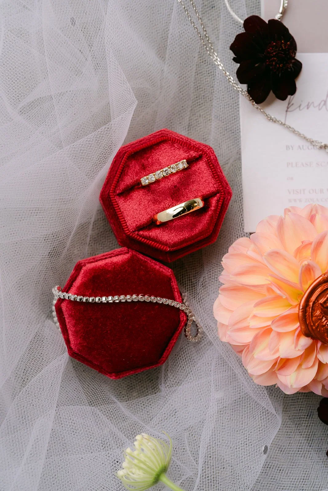 Red octagon ring boxes holding the wedding bands next to a peach dahlia.