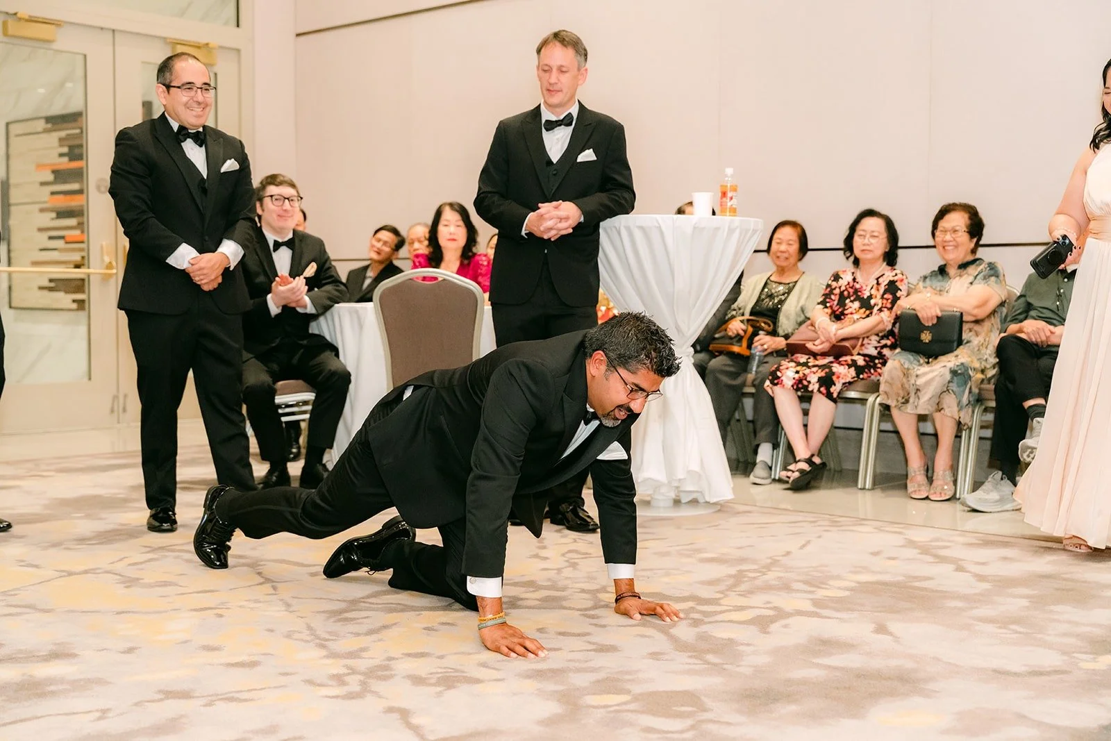 A groomsman doing push ups while guests laugh from their seats