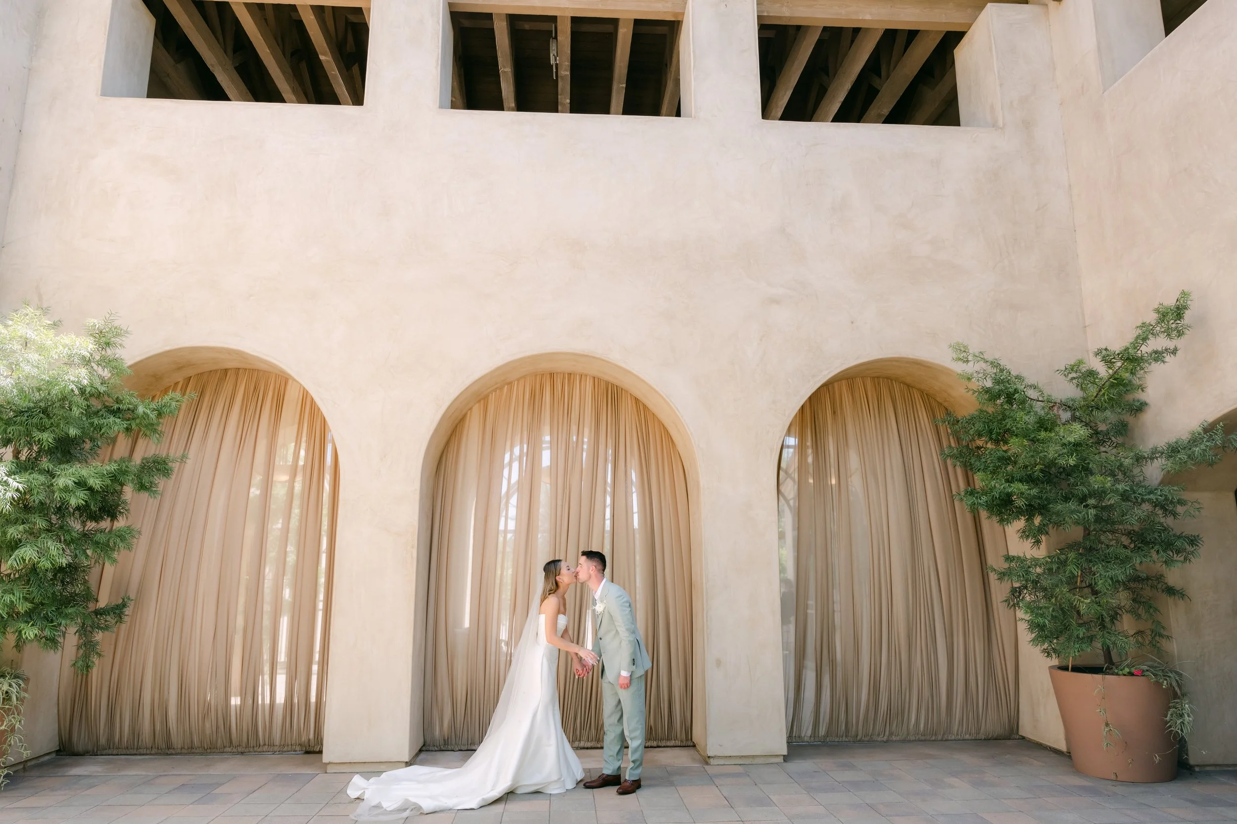 Kieu and Anthony embracing in front of draped arches at Serra Plaza in San Juan Capistrano