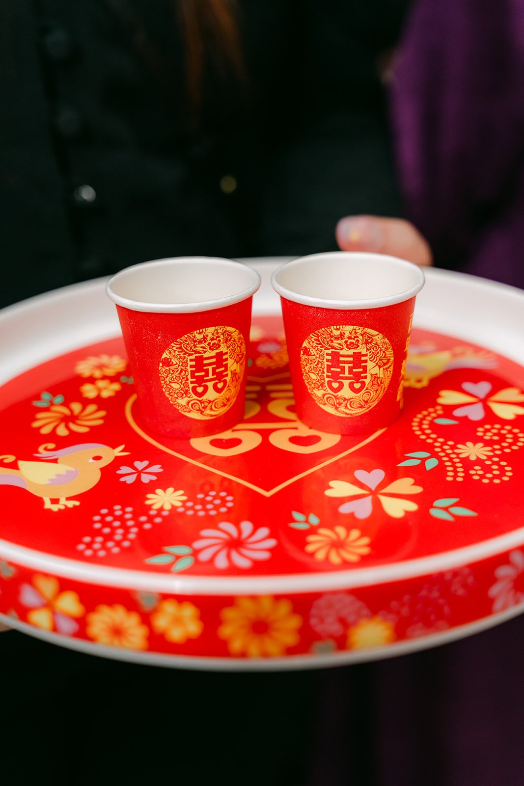 A bridesmaid carrying a red tray with two double happiness teacups.