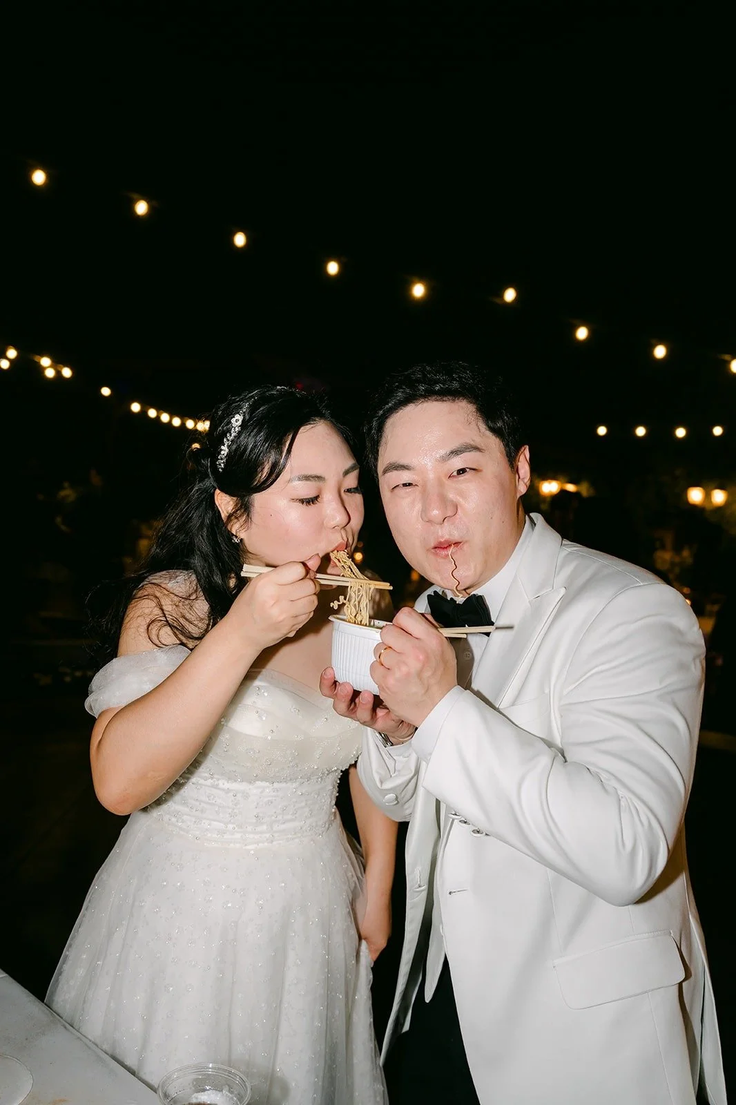 Chorok and Min Soo sharing cup noodles under the string lights, photographed by One and Only Production
