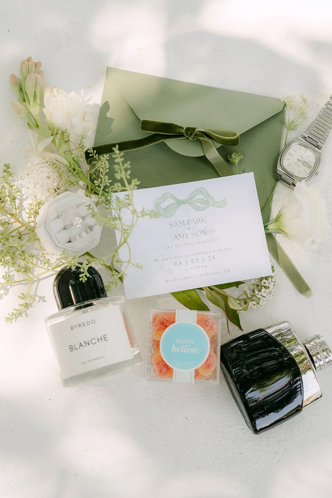 Amy and Sam's sage green invitation suite with perfume and white florals
