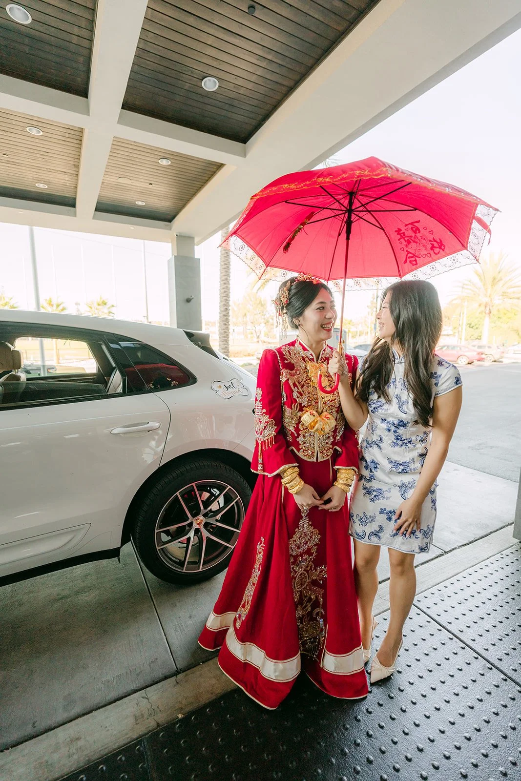 A bridesmaid holding a red umbrella over the bride as she leaves the house.