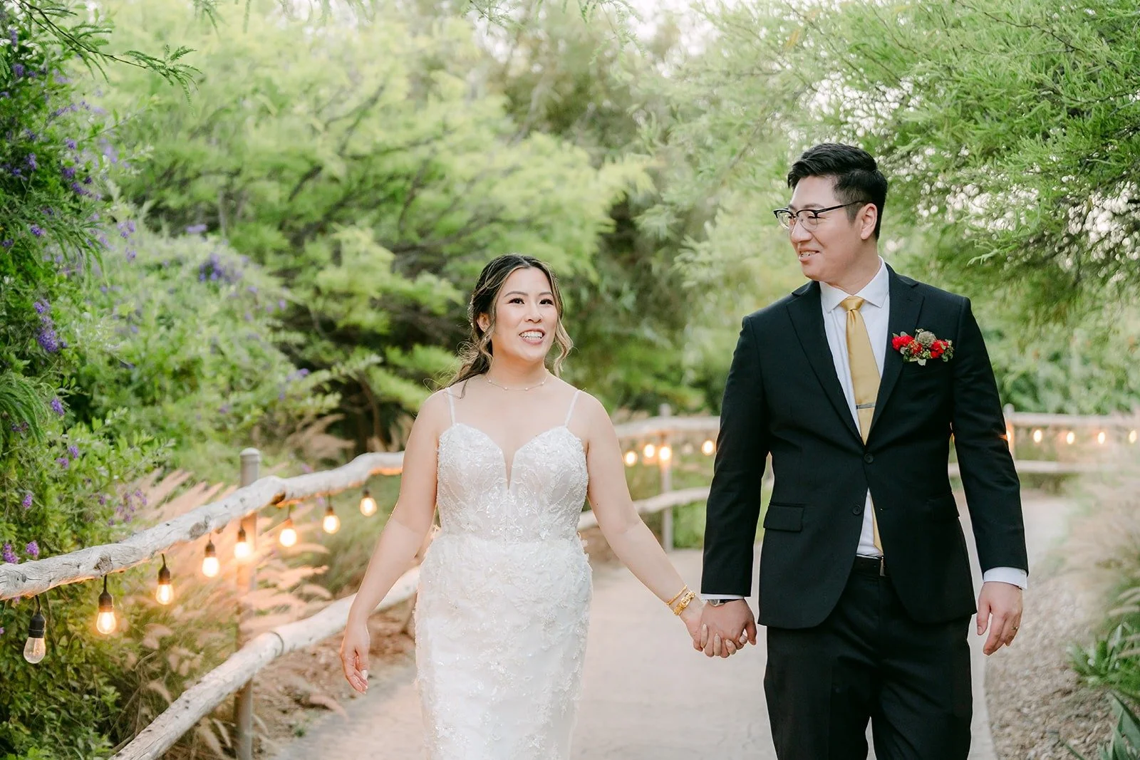 Joanne and Zach walking hand in hand along a lit garden path, photographed by One and Only Production