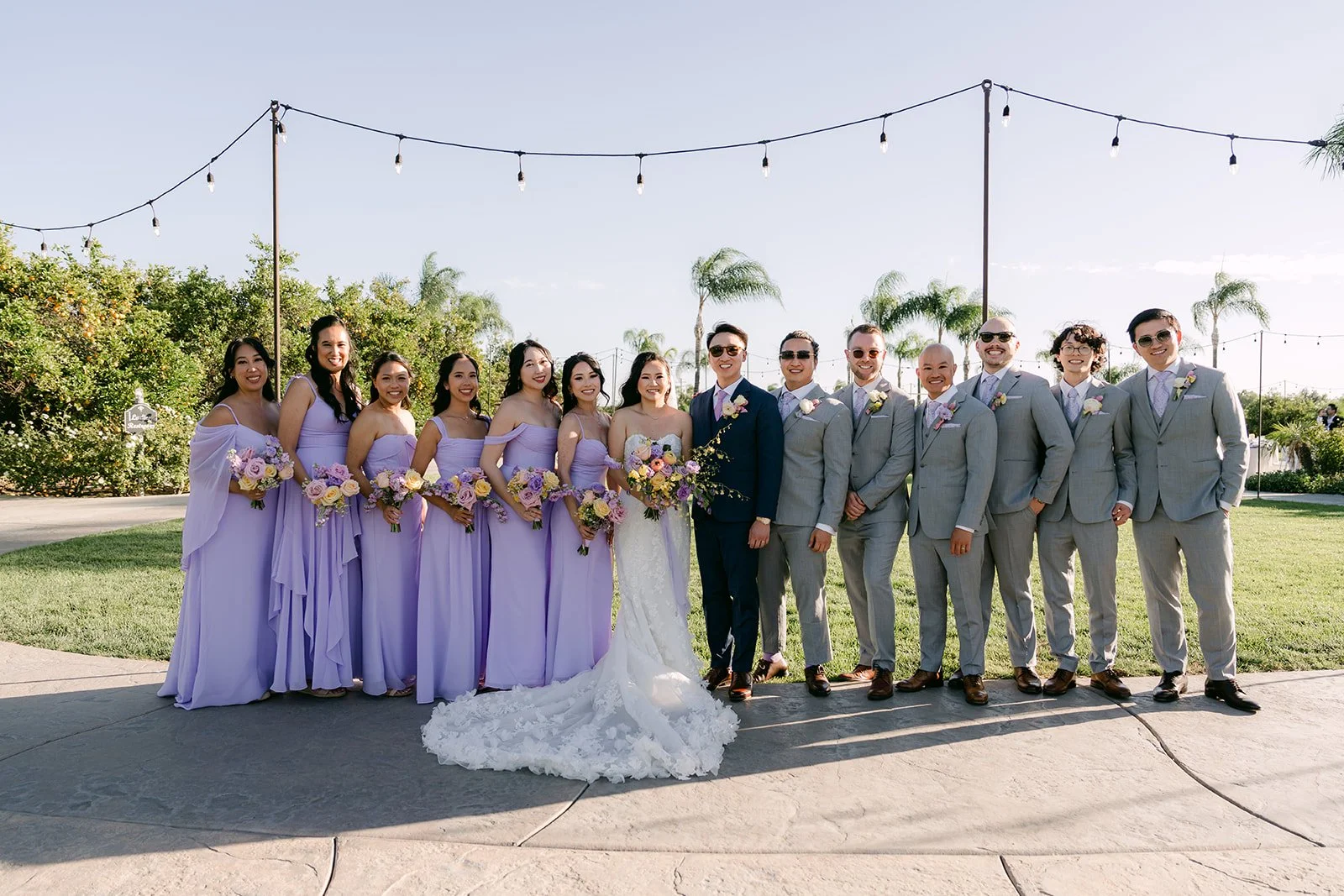 The wedding party on the lawn under the string lights, photographed by One and Only Production.