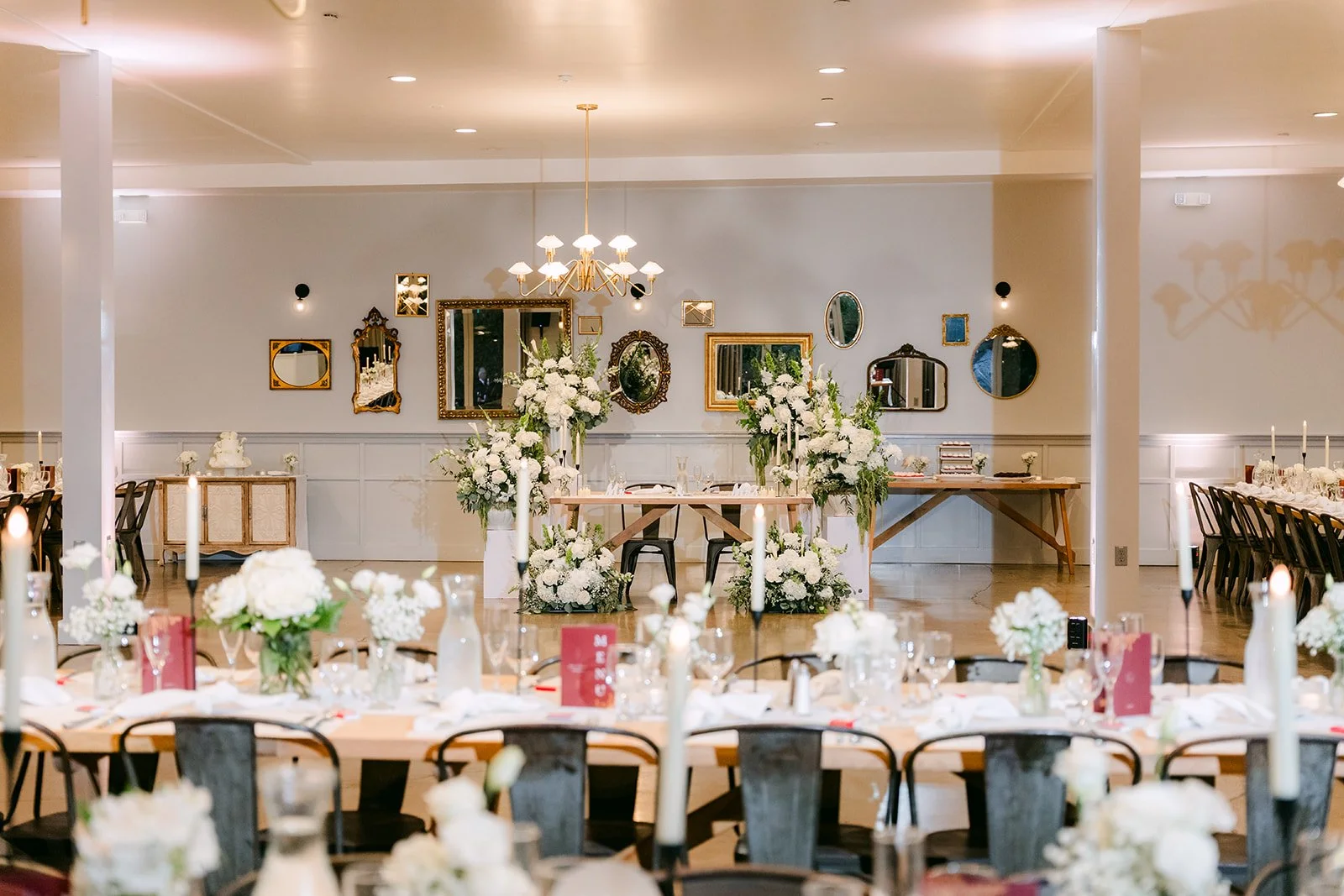 Wide view of the reception room with long tables and chandeliers