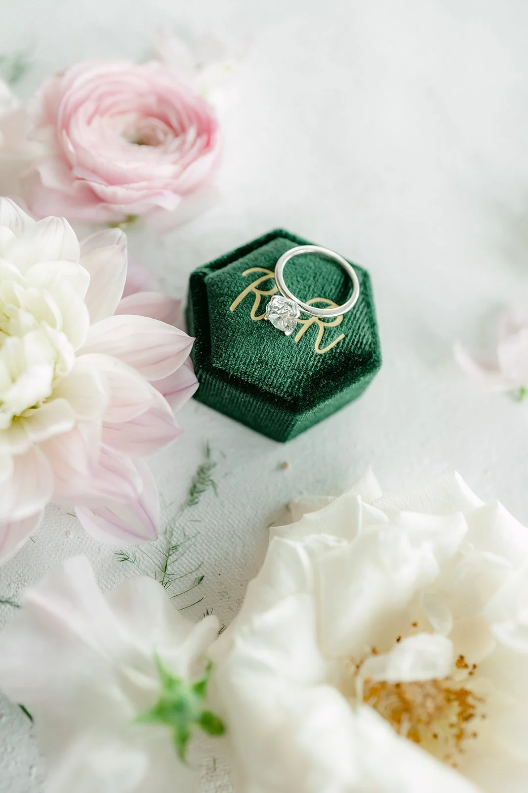 Green velvet ring box with RR monogram among blush ranunculus and ivory roses