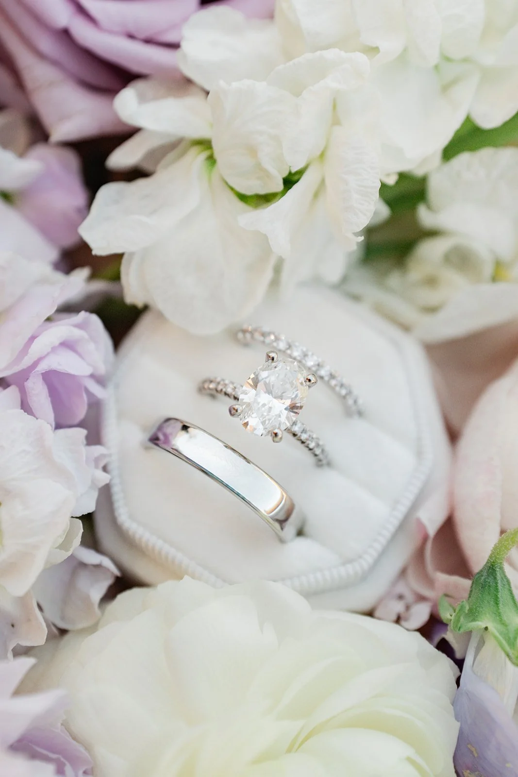 Engagement ring and wedding bands in a ring box among white and lavender flowers