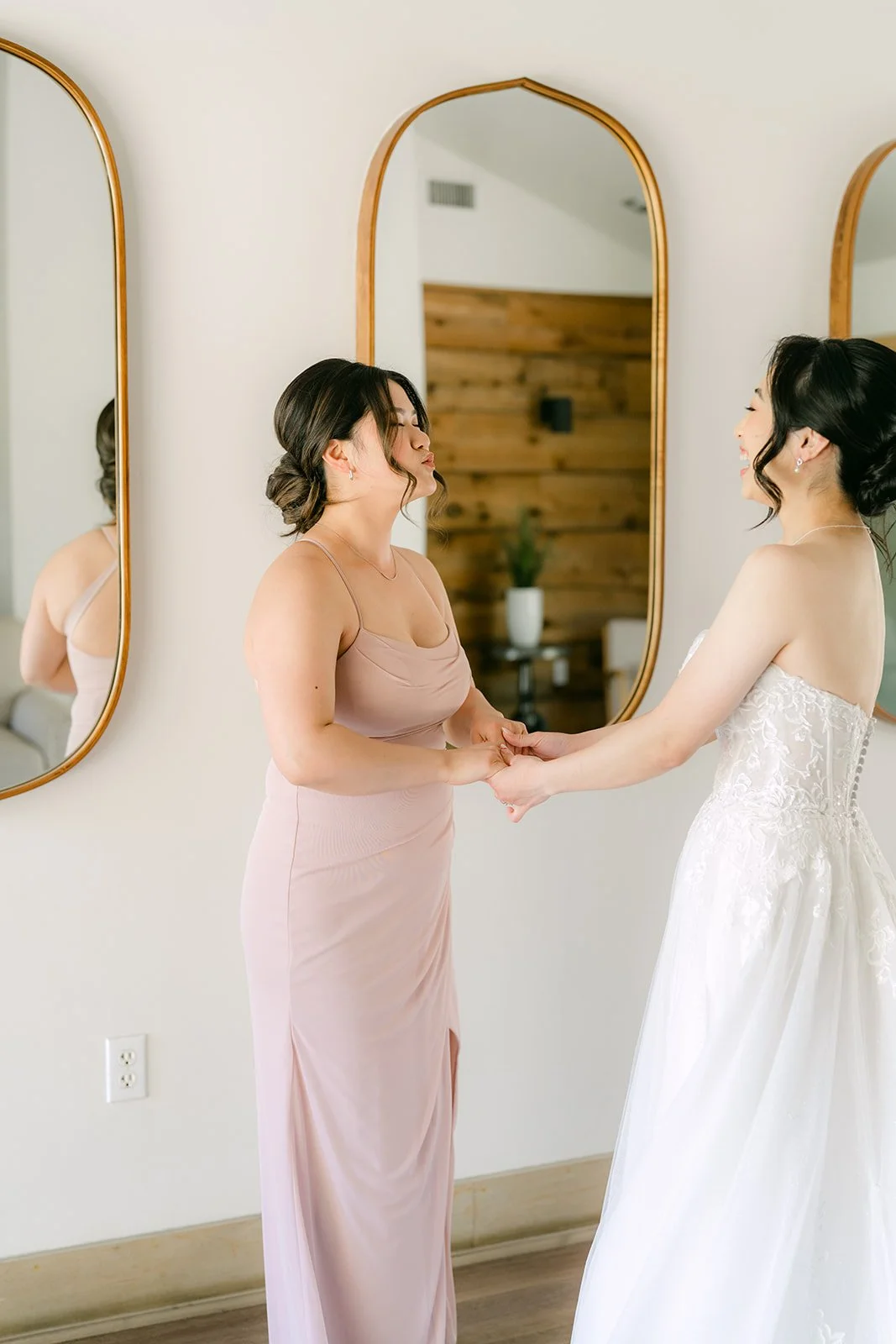 Maid of honor in blush helping the bride into her gown