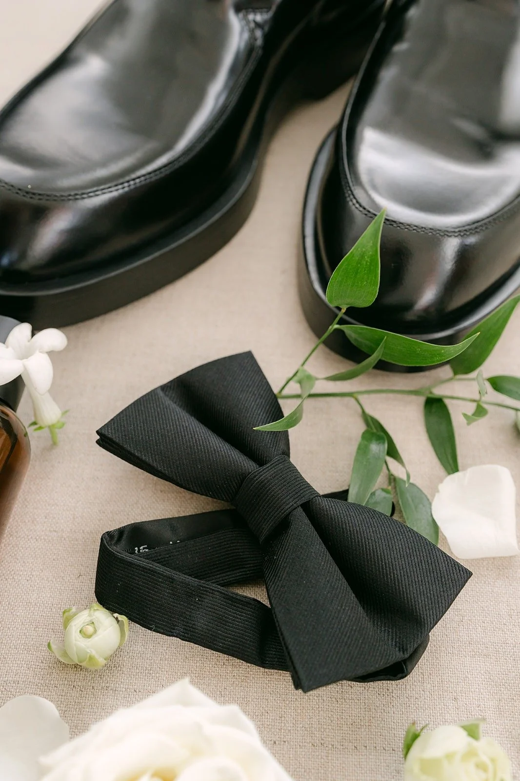 Richard's black shoes and bow tie styled with white roses, photographed by One and Only Production