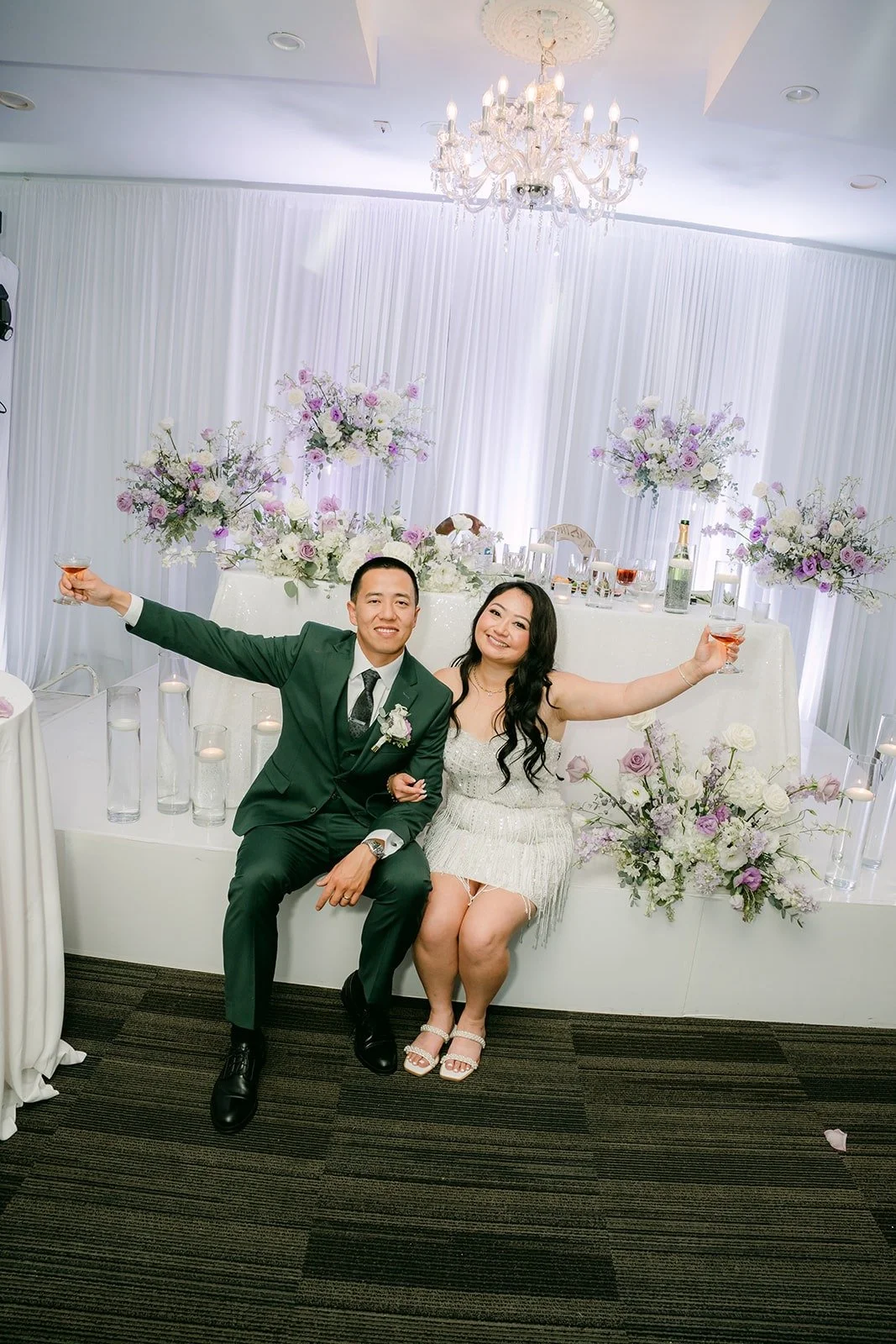 Jennifer and Kevin throw their arms out at the sweetheart table in her second look