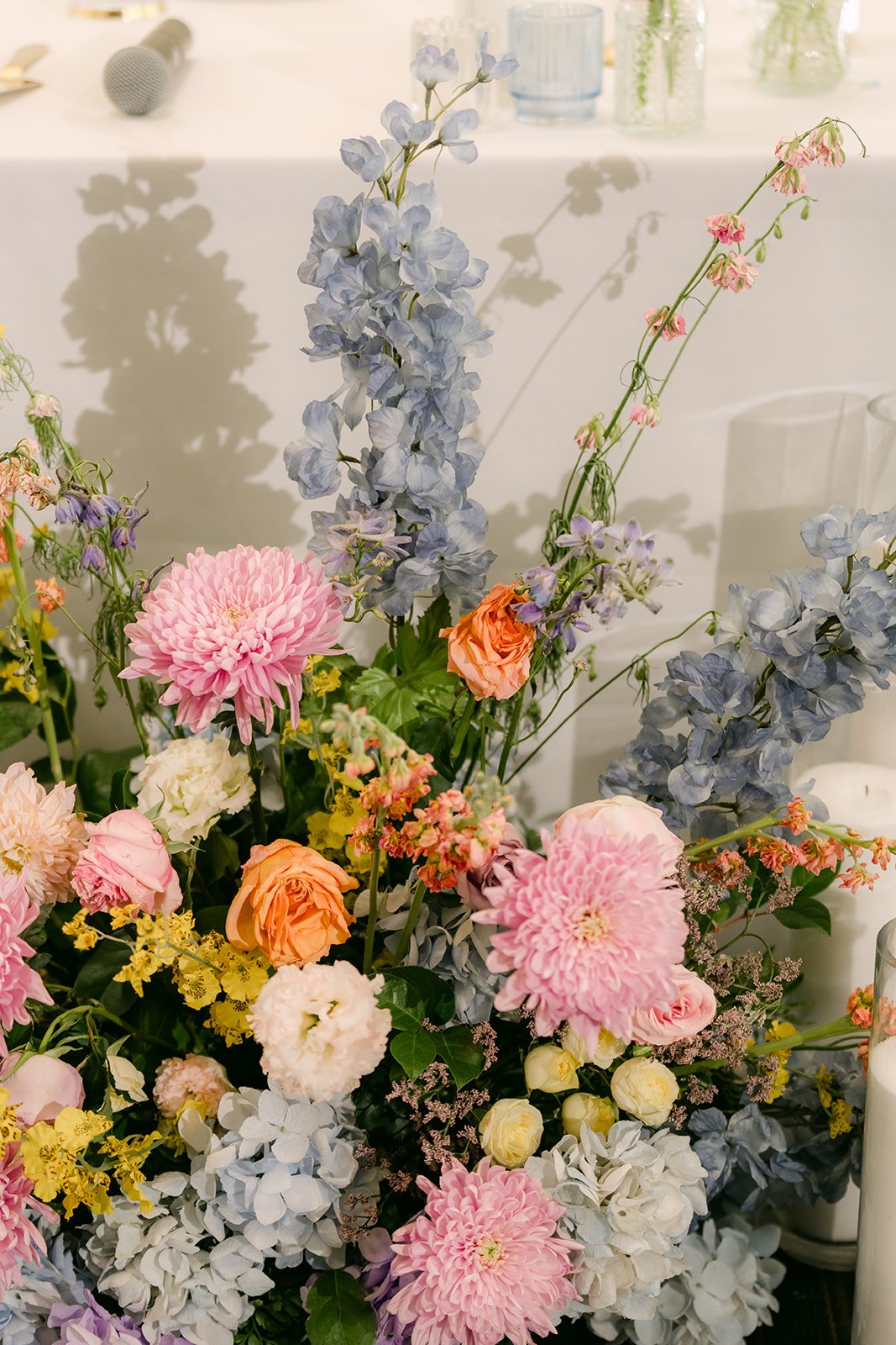 An arrangement of blue delphinium, peach roses and blush blooms by Peonies and Petals.