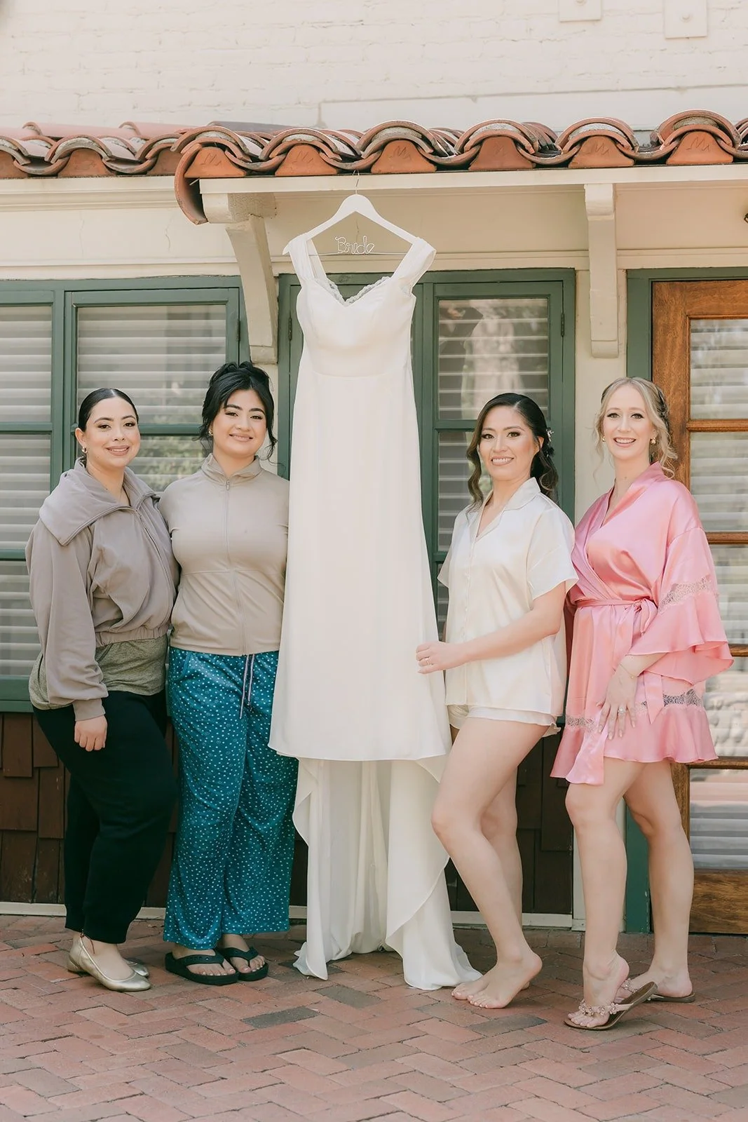 Mariana and her bridesmaids in robes and pajamas beside her hanging wedding gown